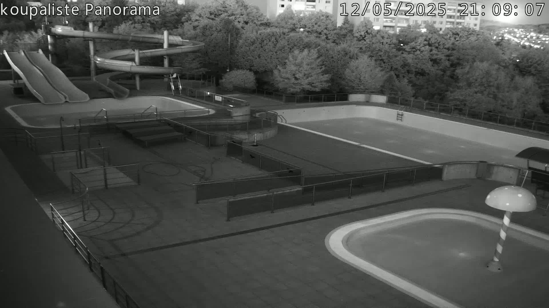 An empty outdoor swimming pool complex at night, featuring water slides and multiple pools of varying sizes, under dark conditions.