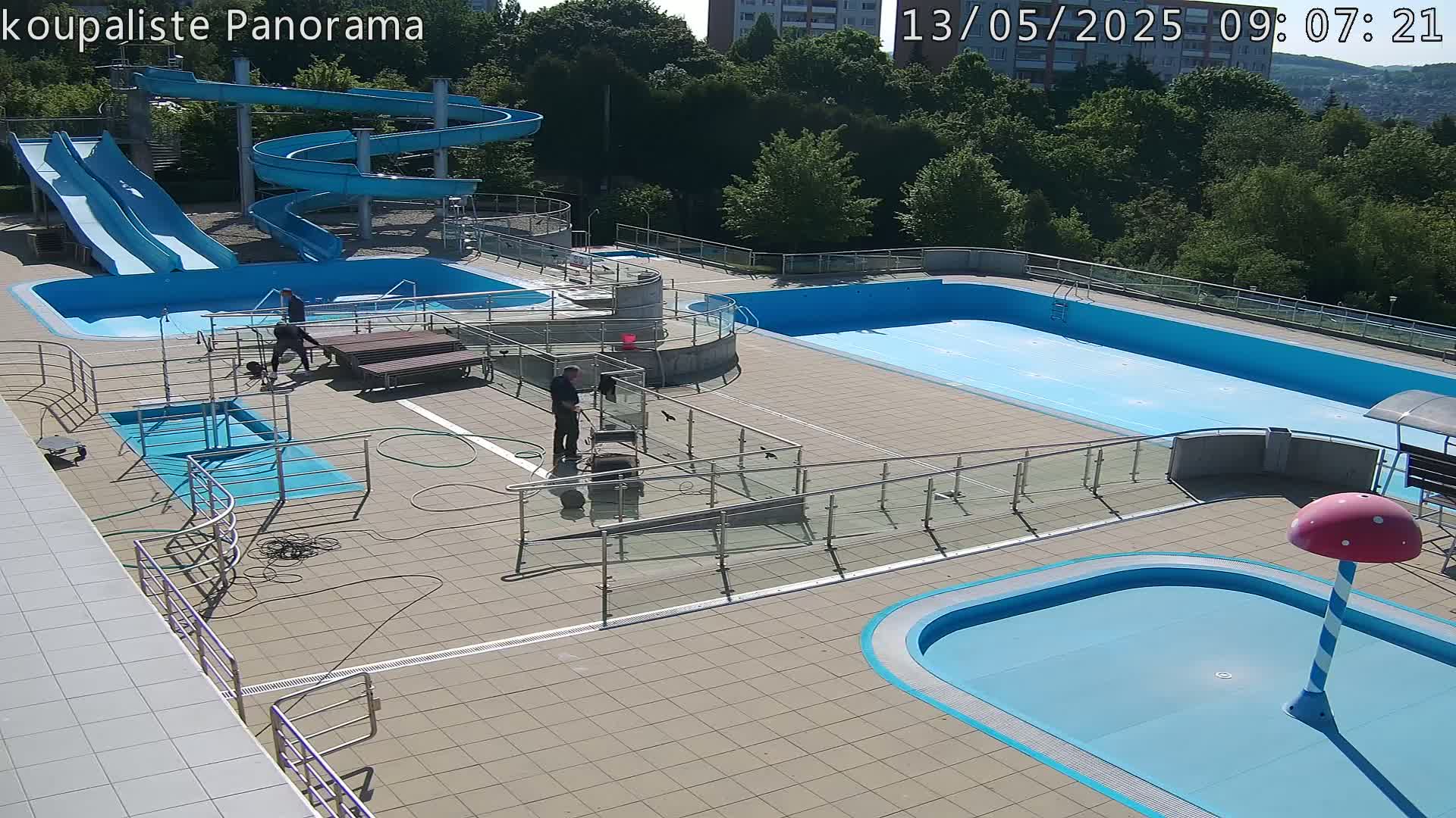An outdoor pool complex with multiple pools, two slides, and several people present on a sunny day.