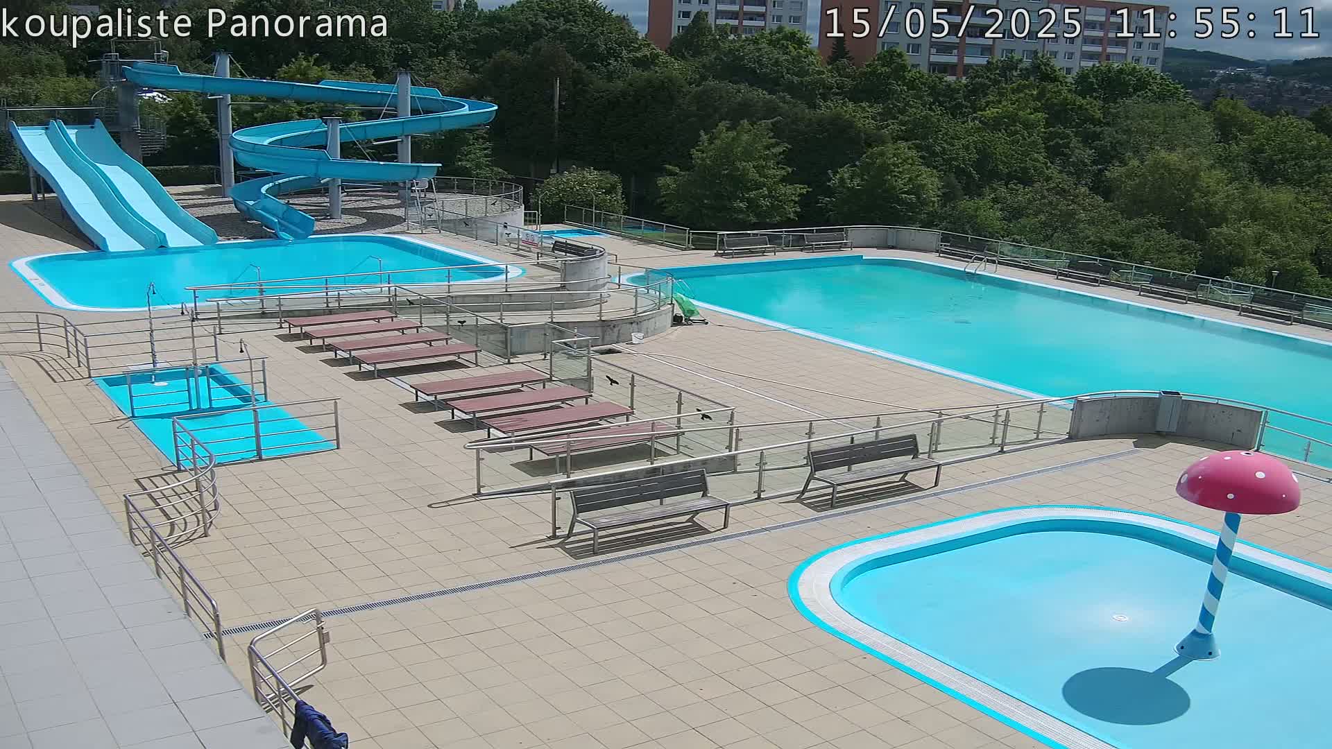 An outdoor pool complex with two large pools, several smaller pools, water slides, and benches, on a sunny day.