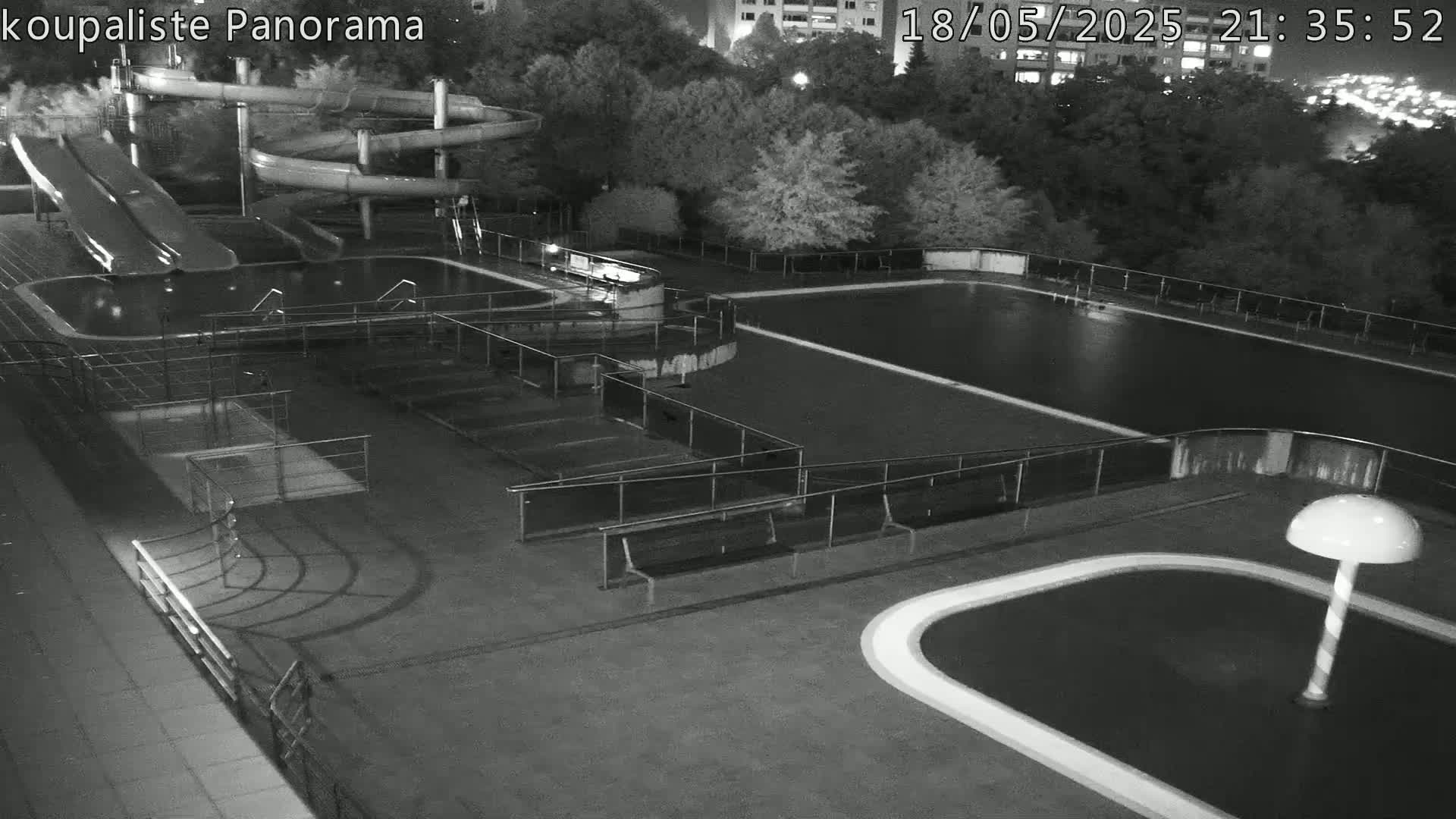 An outdoor nighttime view of an empty swimming pool complex with water slides and benches.