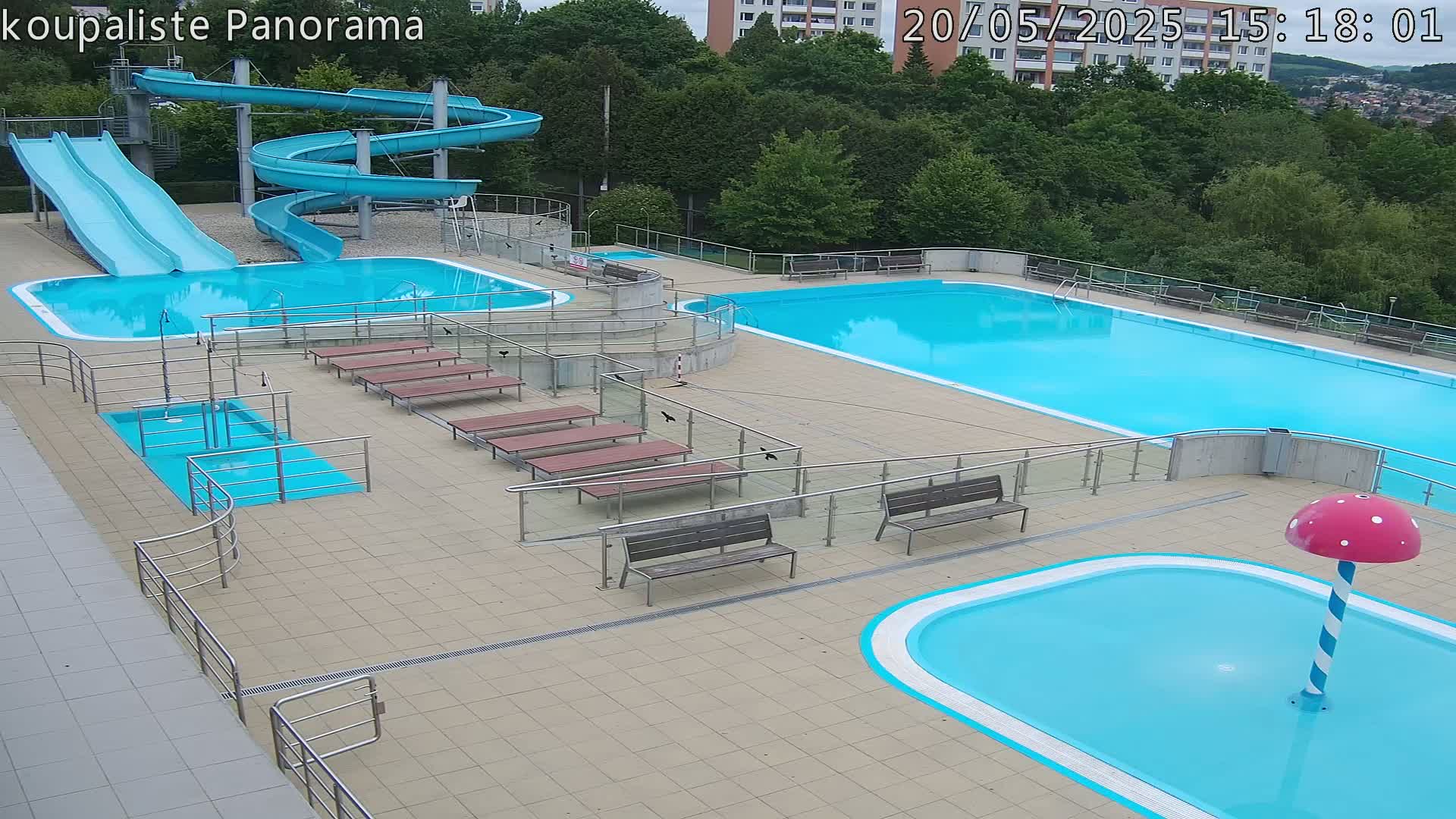 An outdoor swimming complex with multiple pools, water slides, and benches on a sunny day.