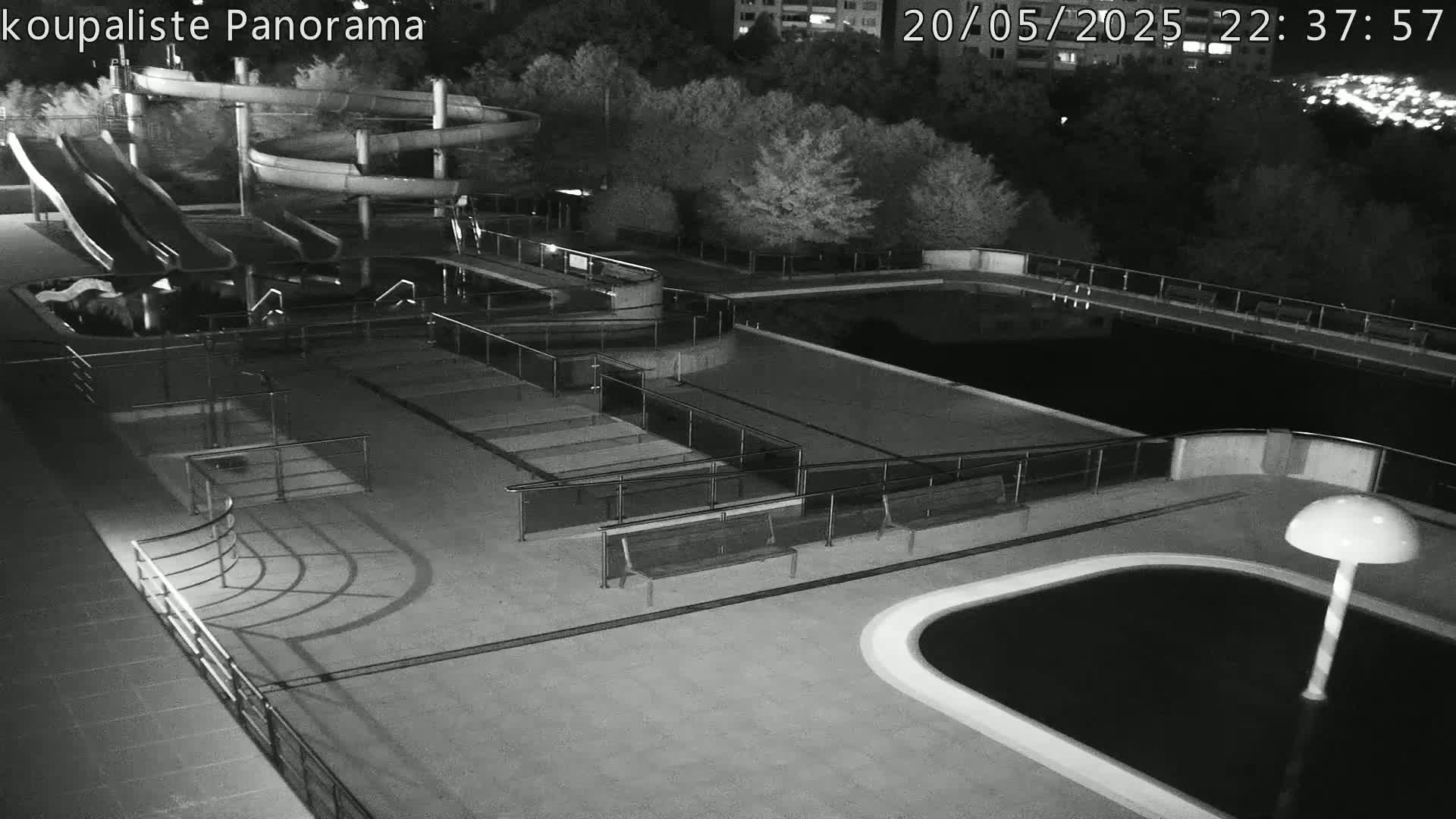 An outdoor swimming pool complex with water slides is shown at night under dark conditions.