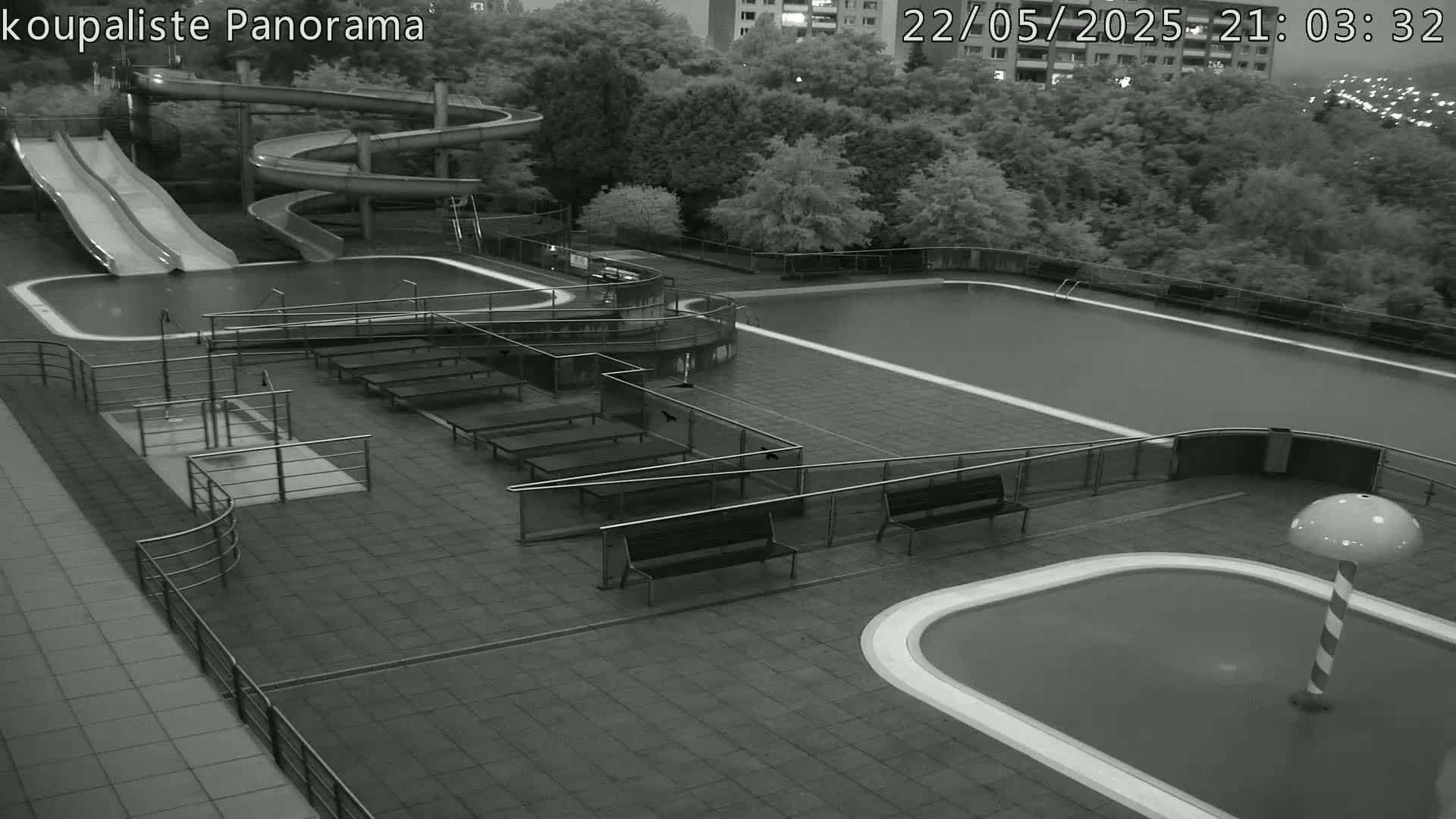 An outdoor nighttime view of an empty swimming pool complex with water slides, benches, and a small wading pool.
