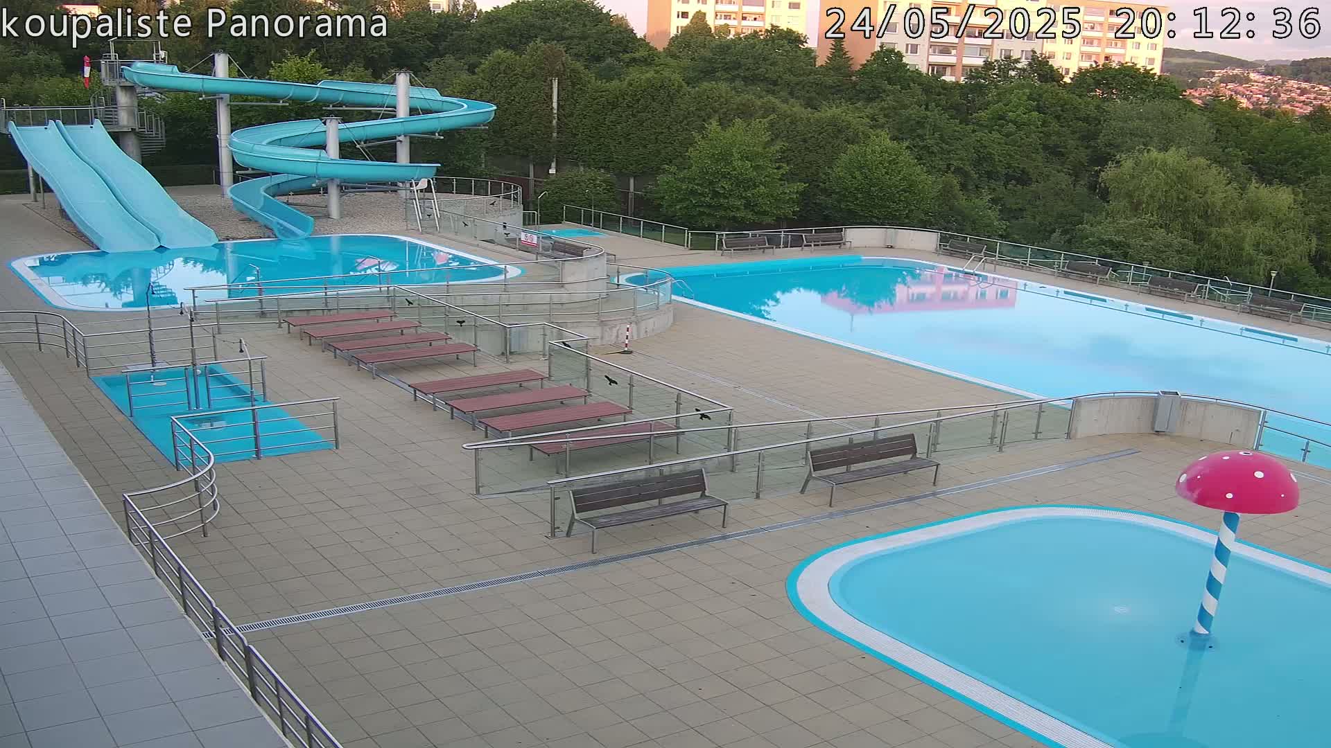 An outdoor pool complex with two large pools, a smaller children's pool with a mushroom-shaped fountain, and two water slides.