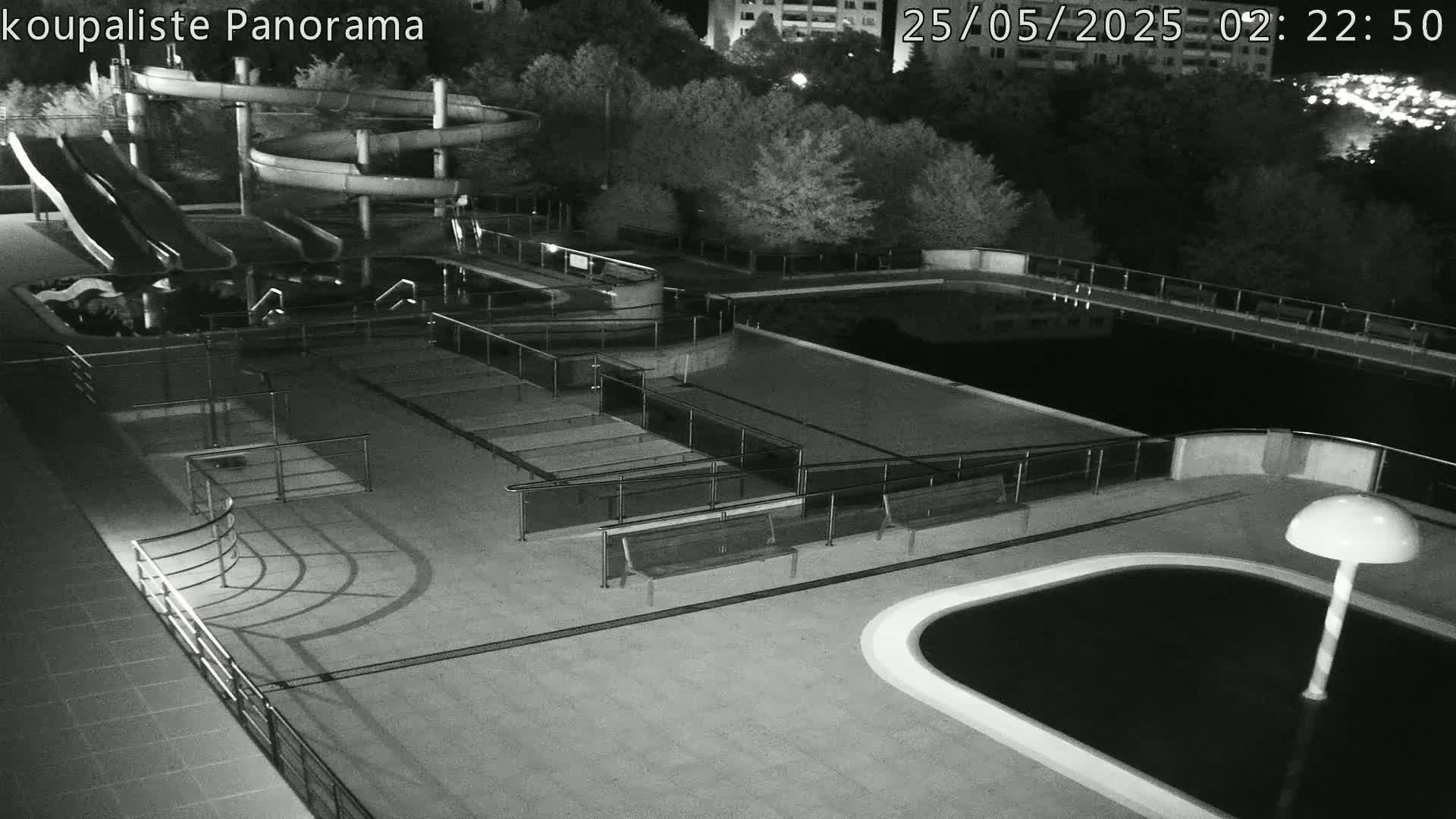 An outdoor nighttime view of an empty swimming pool complex with water slides and benches.