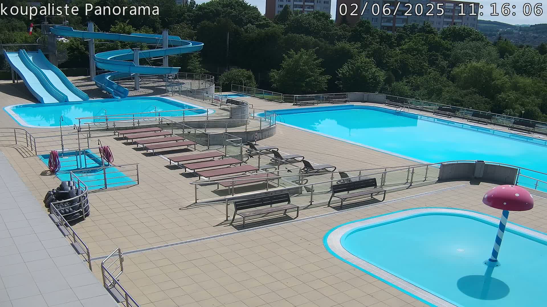 An outdoor pool complex with multiple pools, water slides, and benches on a sunny day.