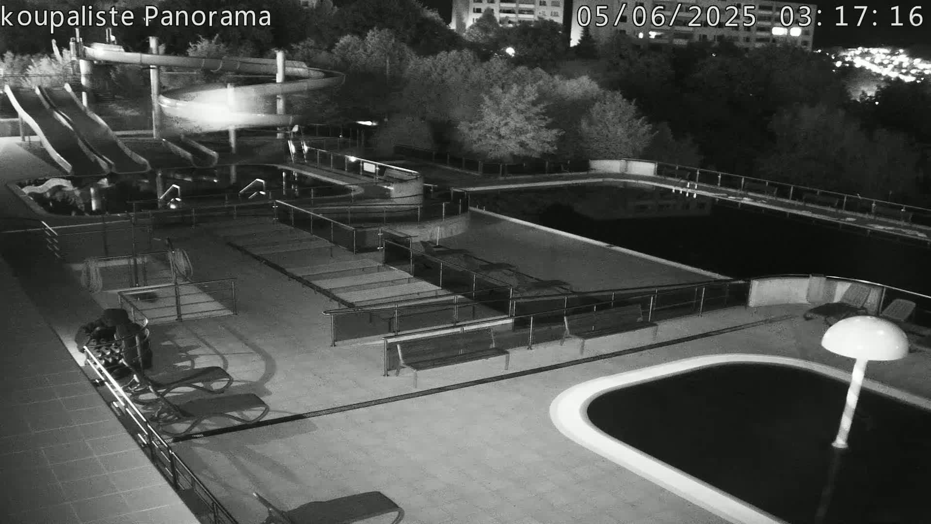 An outdoor nighttime view of an empty swimming complex with multiple pools, water slides, and lounge chairs.