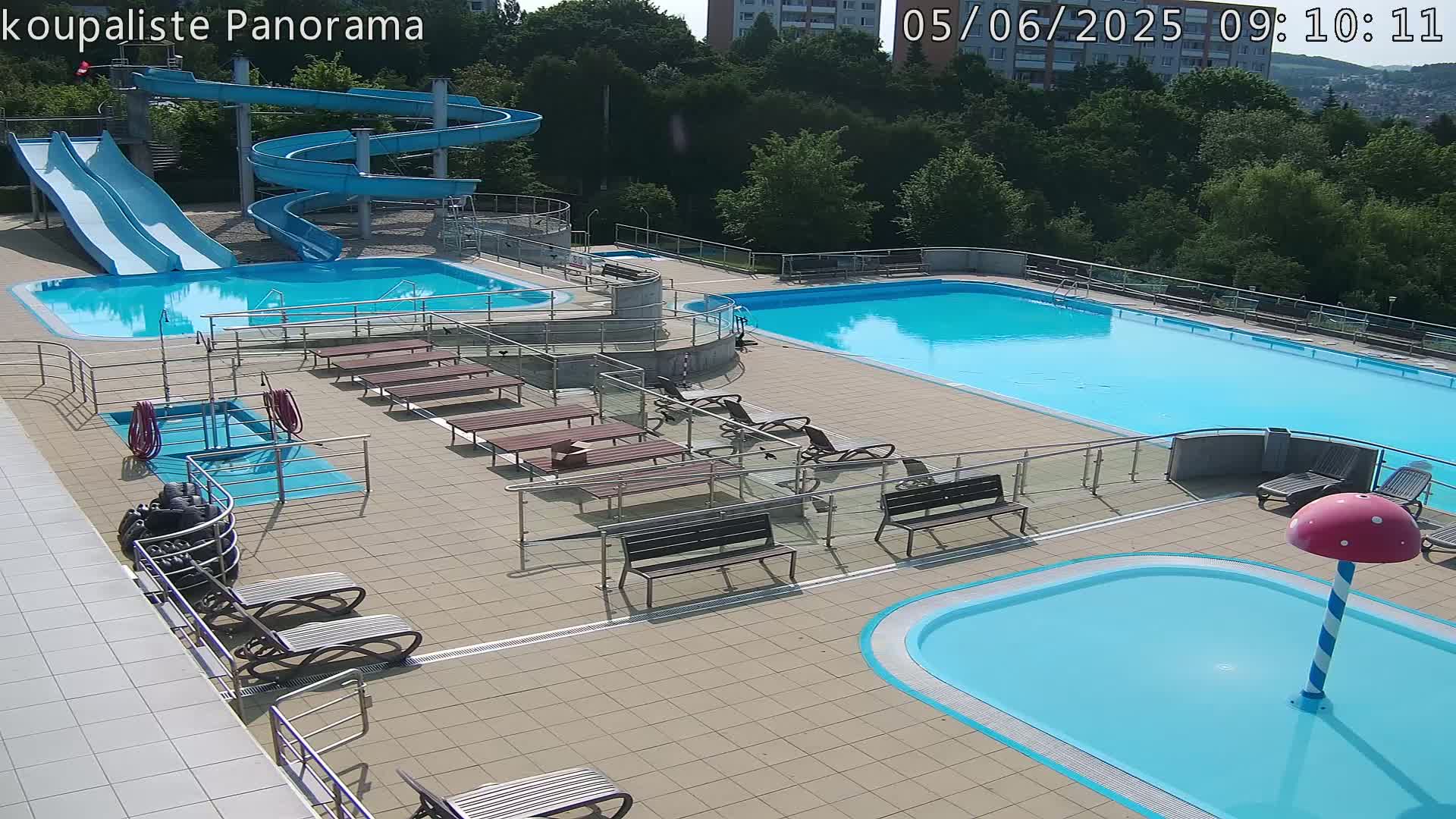 An outdoor swimming complex with multiple pools, slides, and lounge chairs on a sunny day.