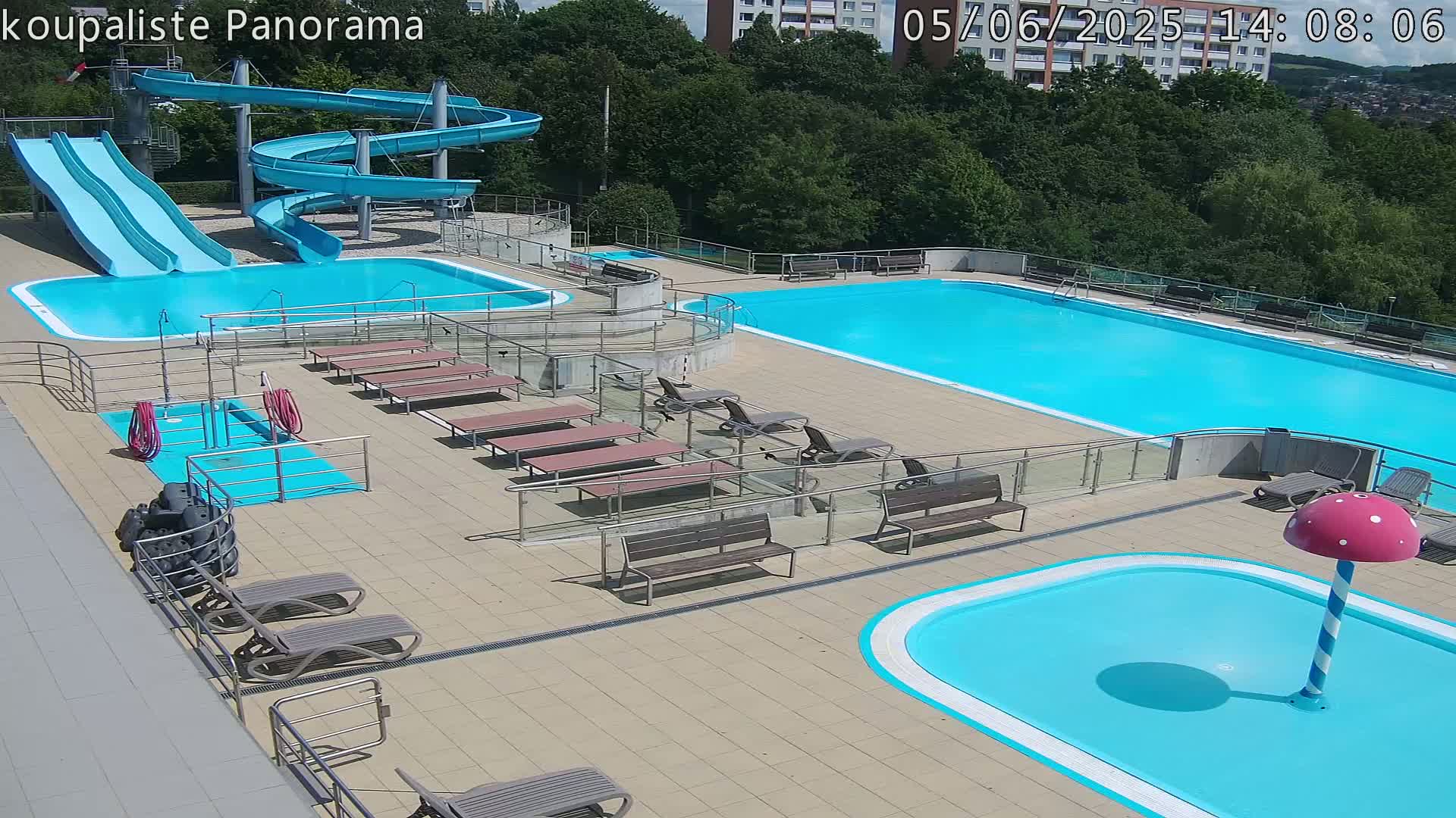 An outdoor swimming complex with multiple pools, water slides, lounge chairs, and benches on a sunny day.