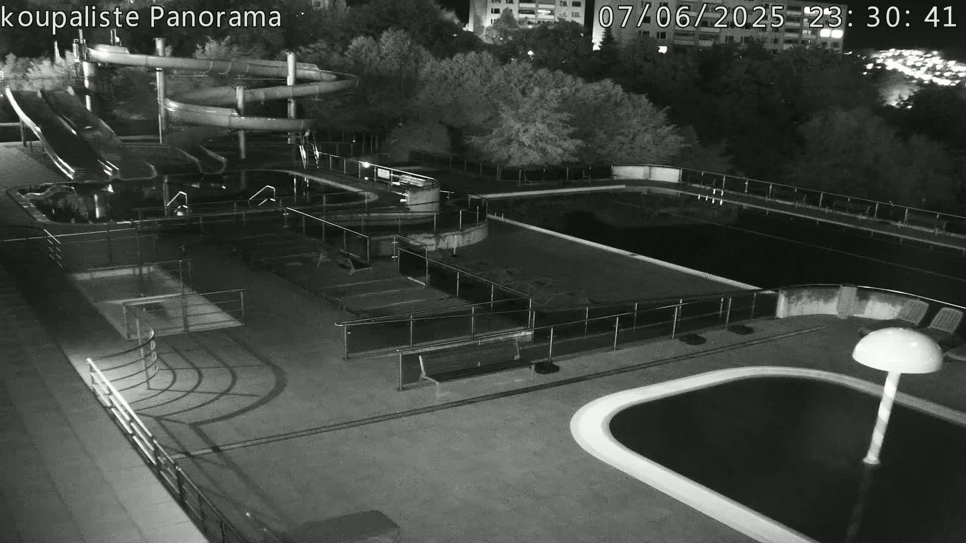 An outdoor swimming complex at night, showing several pools, water slides, and benches, under dark conditions.