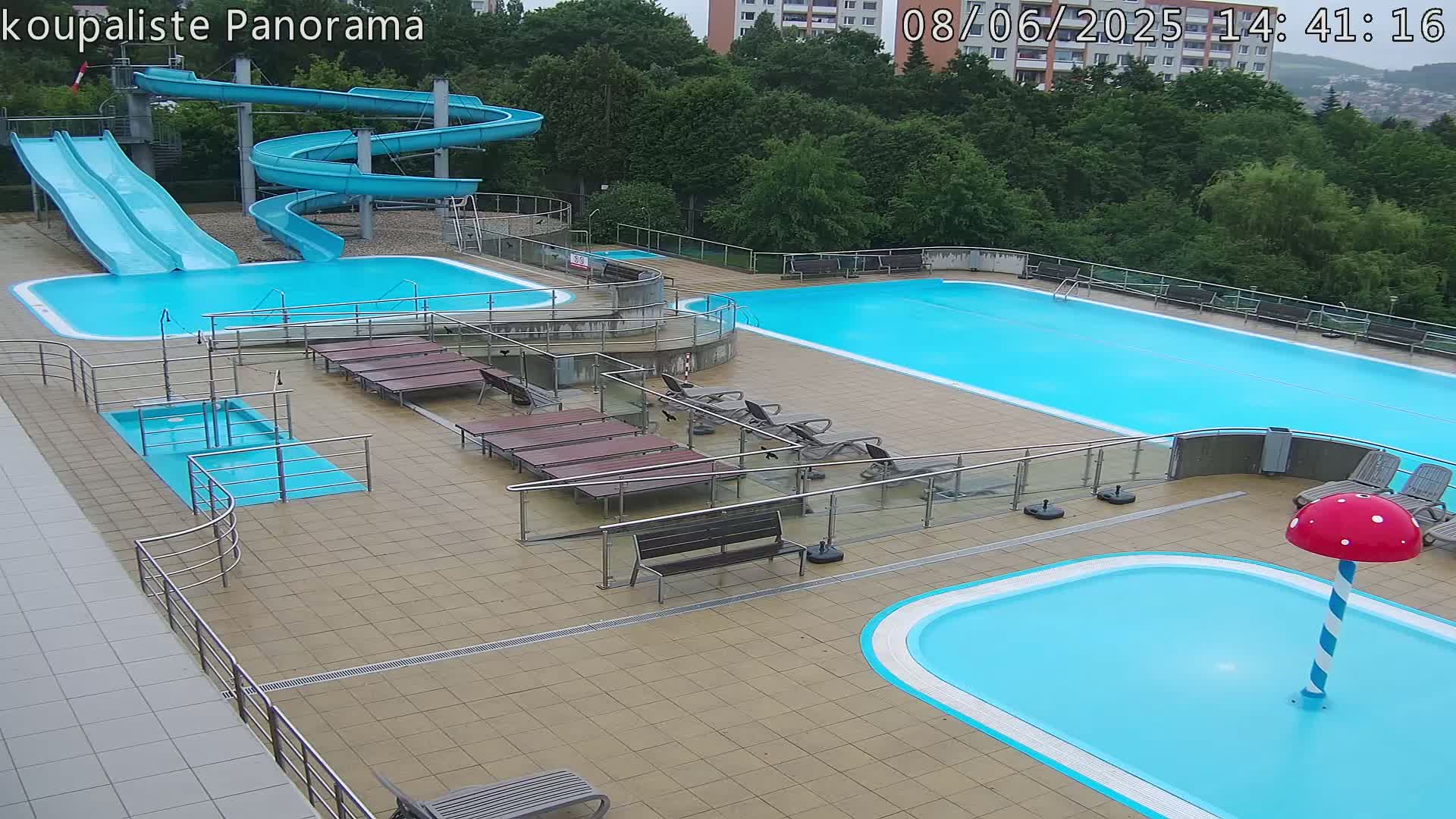 An outdoor swimming complex with multiple pools, slides, and lounge chairs on a mostly sunny day.