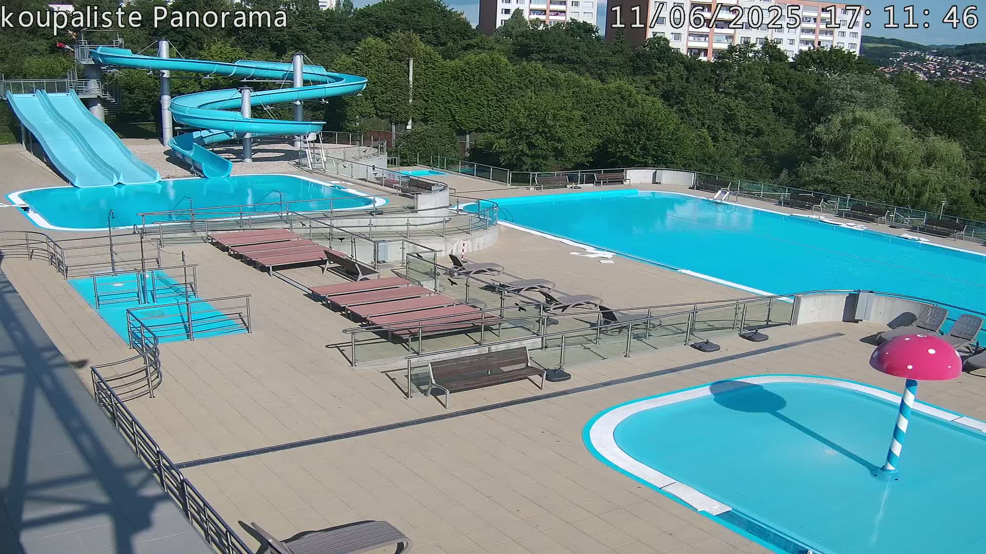 An outdoor swimming complex with multiple pools, water slides, and lounge chairs on a sunny day.