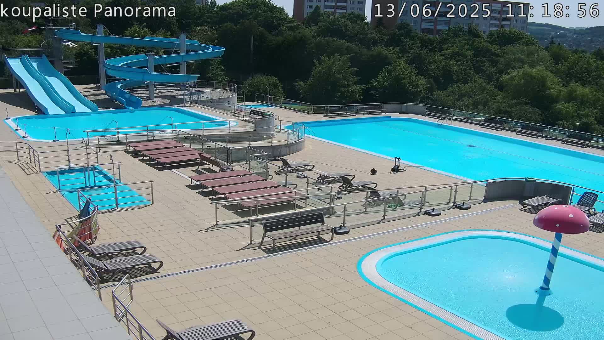An outdoor pool complex with multiple pools, water slides, lounge chairs, and a mushroom-shaped water feature on a sunny day.