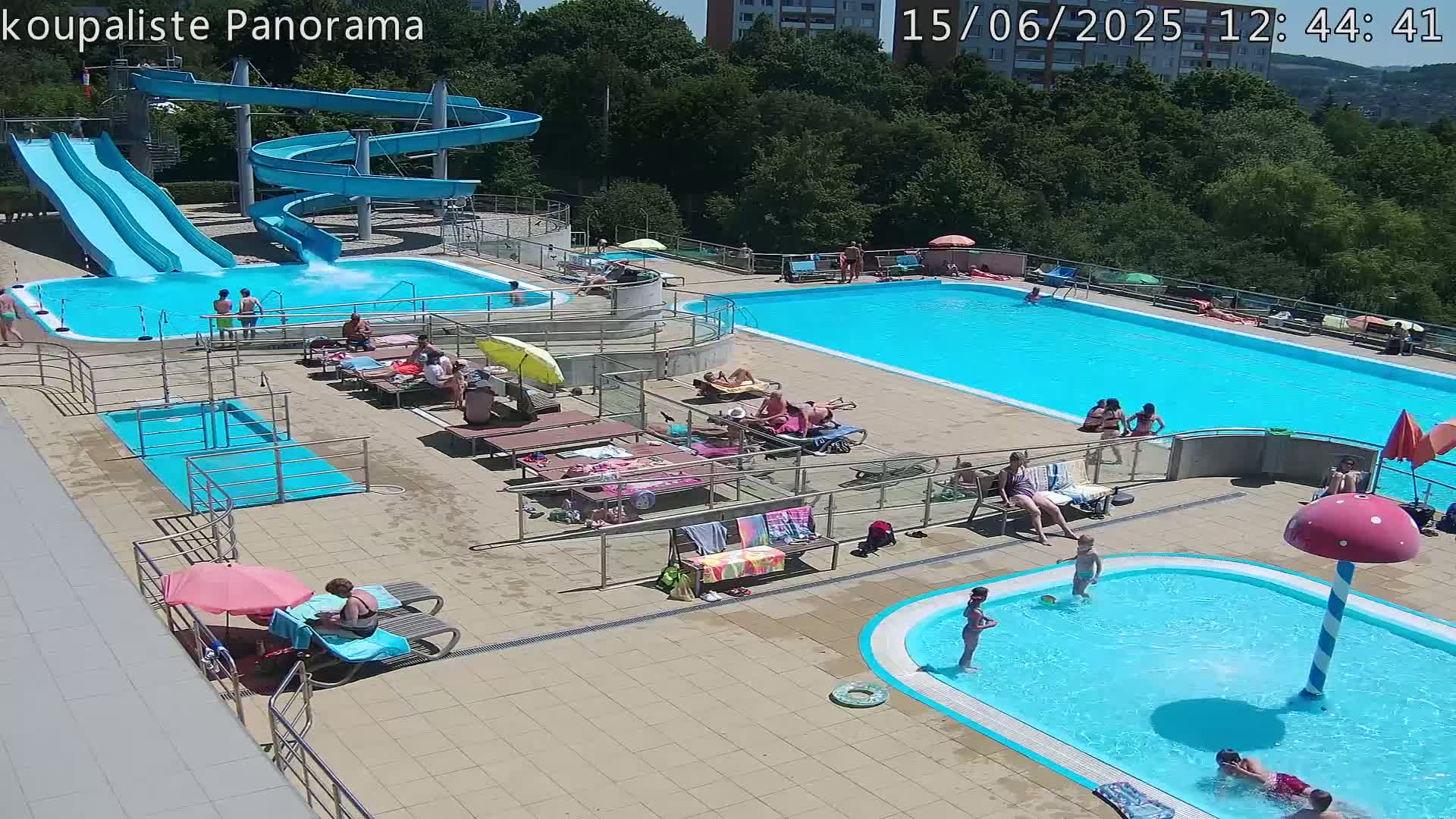 An outdoor pool complex with multiple pools, water slides, and sunbathers on a sunny day.