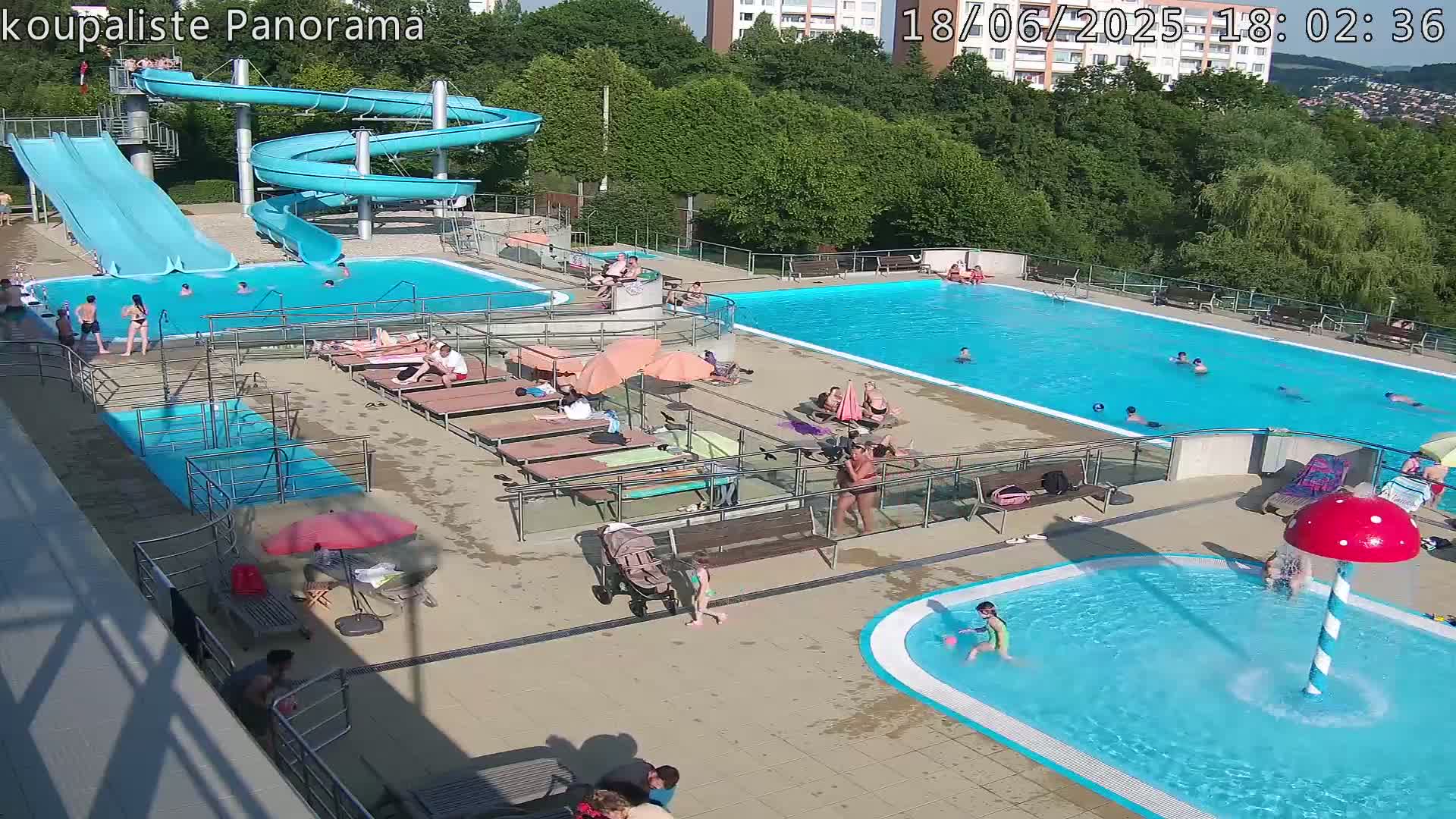 An outdoor swimming pool complex with multiple pools, slides, and sunbathers on a sunny day.