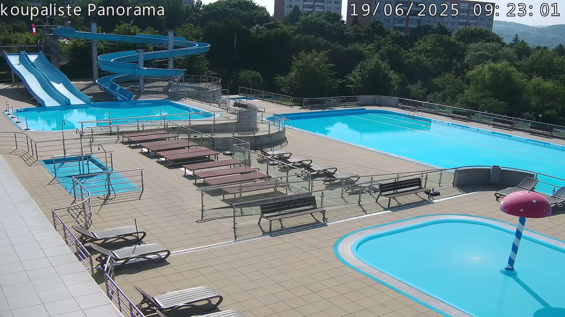 An outdoor pool complex with several pools of varying sizes, slides, and lounge chairs on a sunny day.