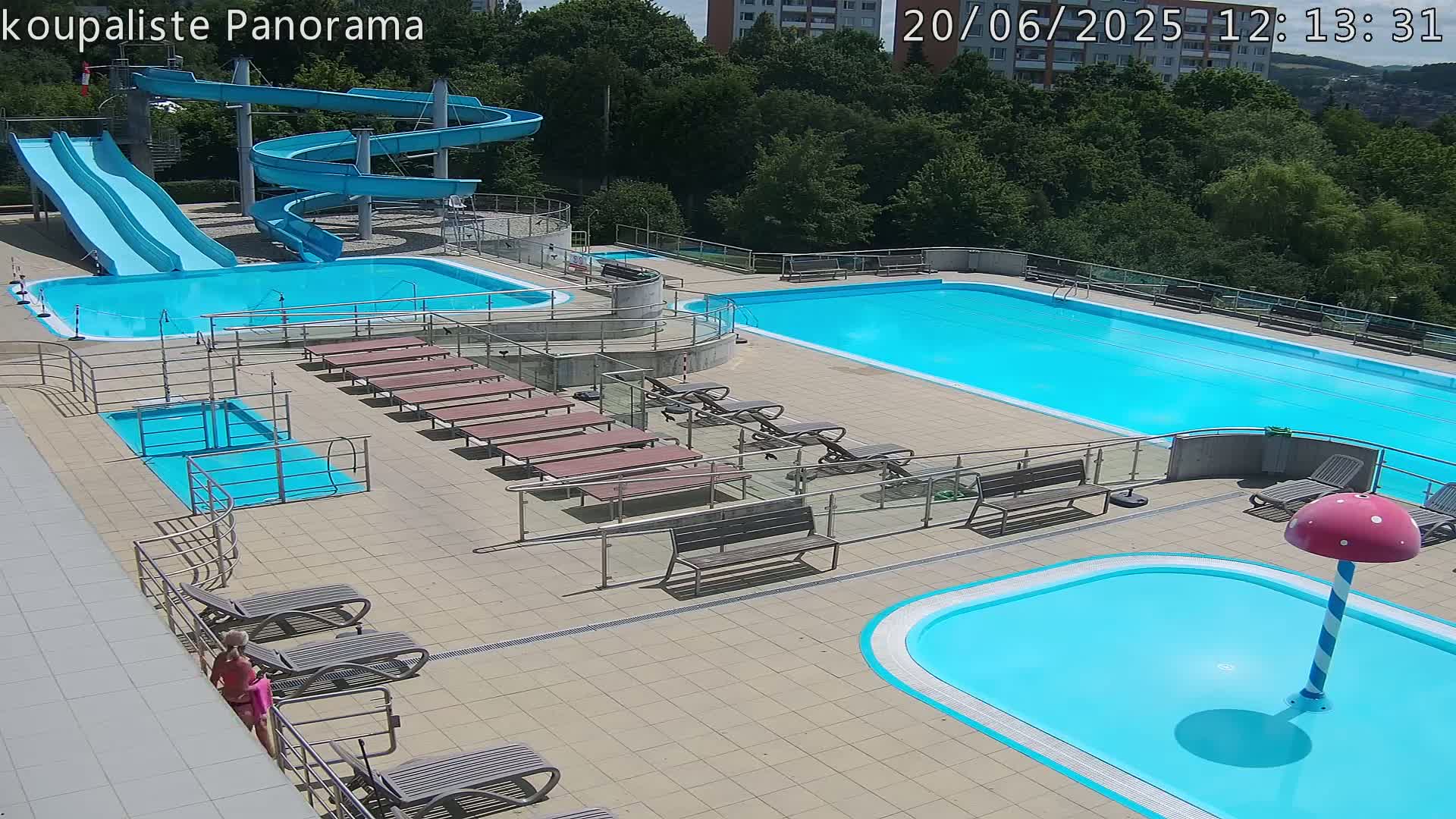 An outdoor swimming complex with multiple pools, water slides, and lounge chairs on a sunny day.