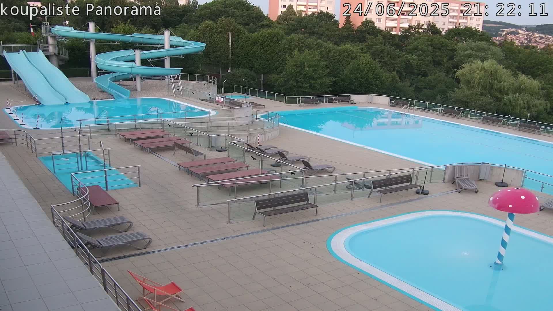 An outdoor pool complex with multiple pools, slides, and lounge chairs under a clear evening sky.