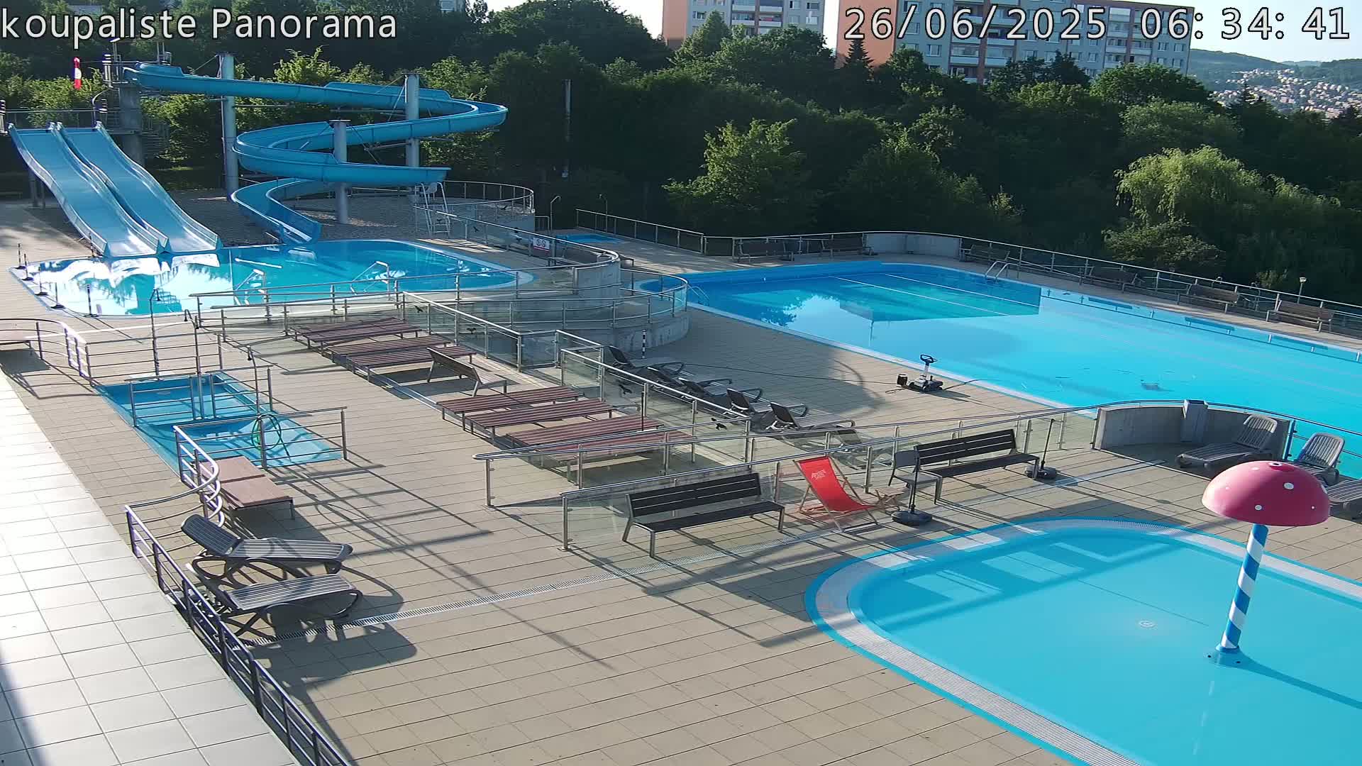 An outdoor pool complex with multiple pools, slides, and lounge chairs under a clear evening sky.