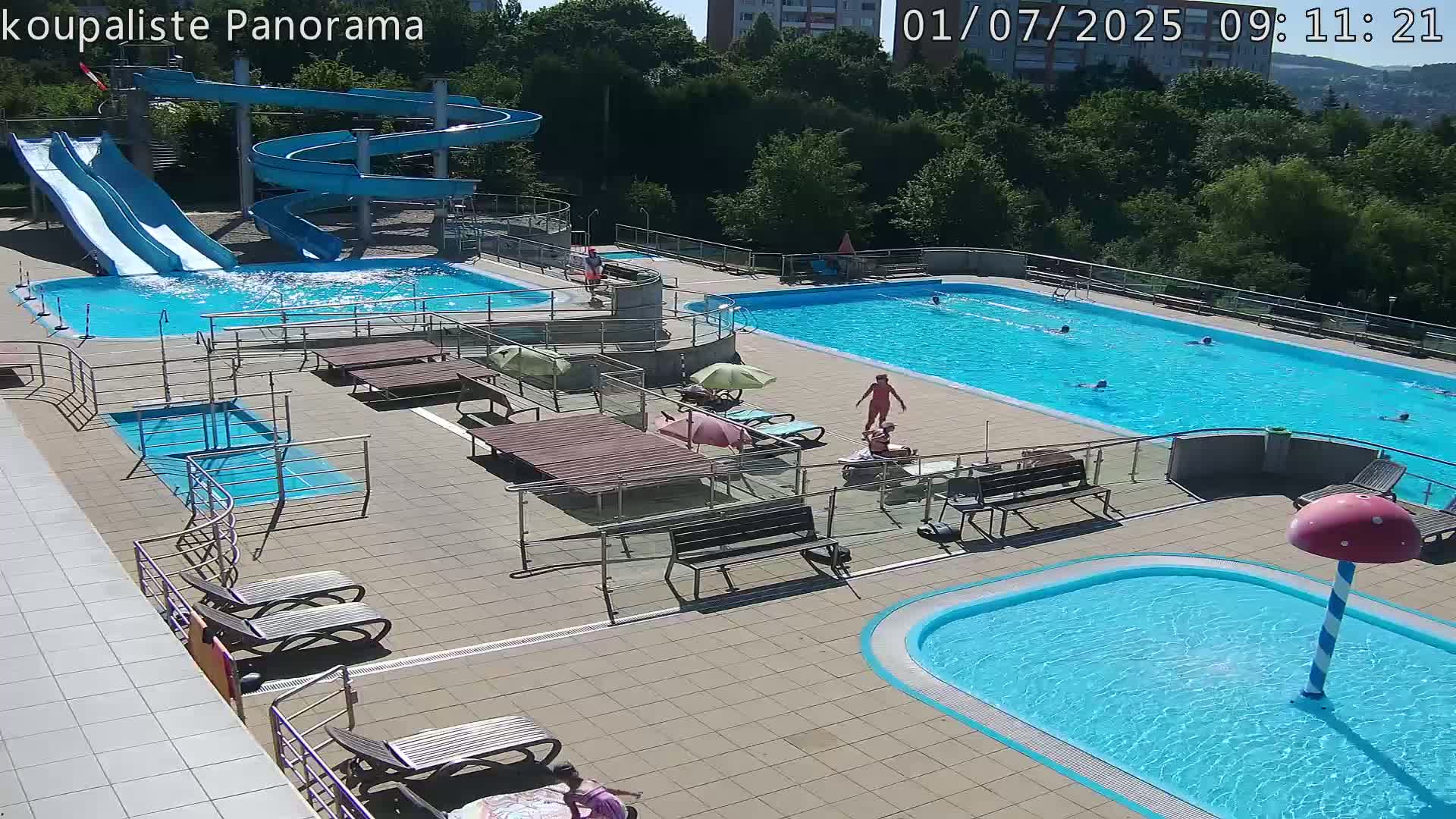 An outdoor pool complex with multiple pools, water slides, and lounge chairs on a sunny day.