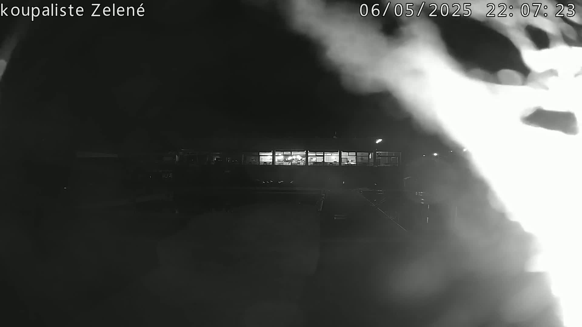 A nighttime, blurry, black-and-white image shows a brightly lit building in the distance, partially obscured by fog or steam.