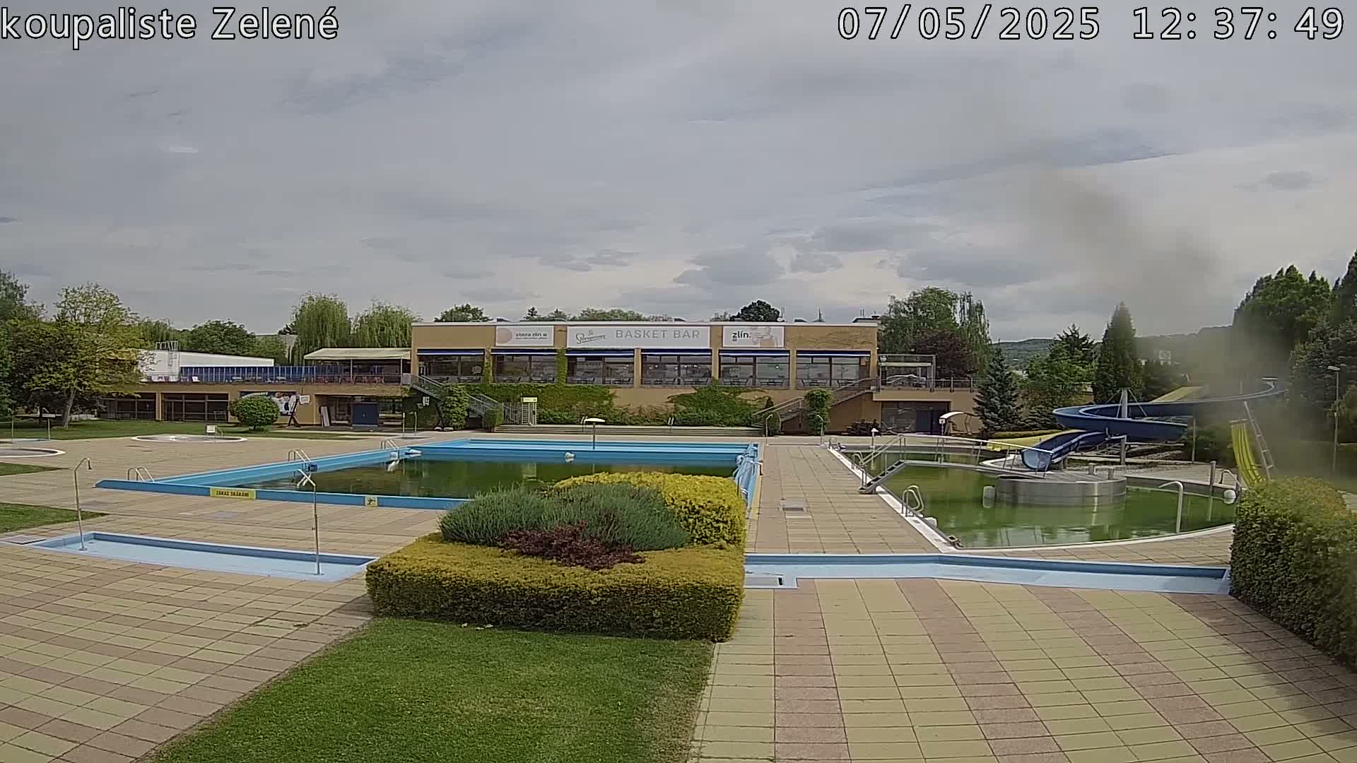 An outdoor pool complex with a building, several pools, and water slides under a cloudy sky.