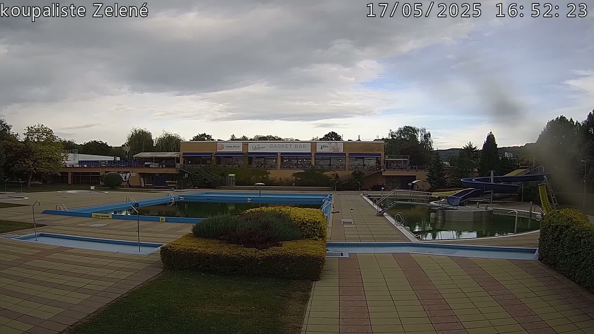An outdoor swimming pool complex with a building and water slides under a partly cloudy sky.
