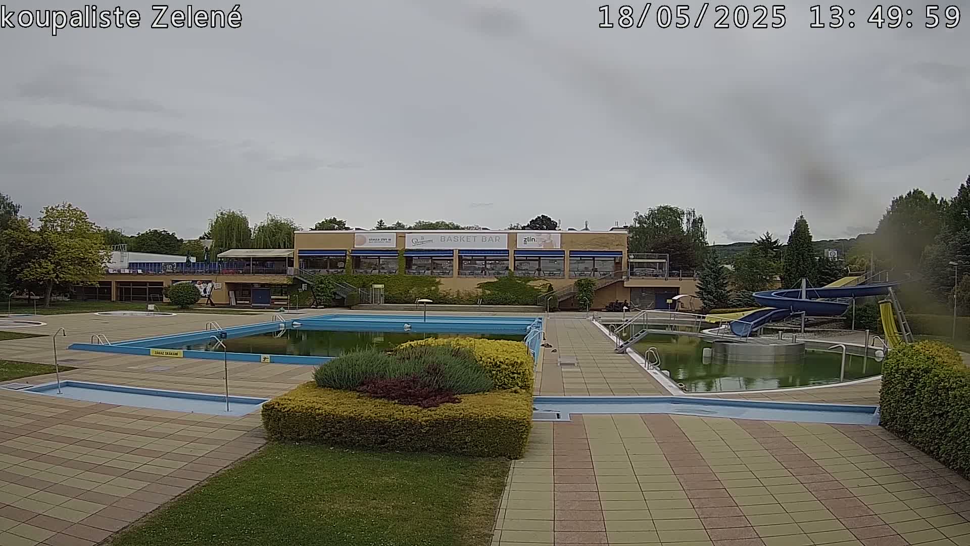 An outdoor swimming pool complex with a building and water slides, under an overcast sky.