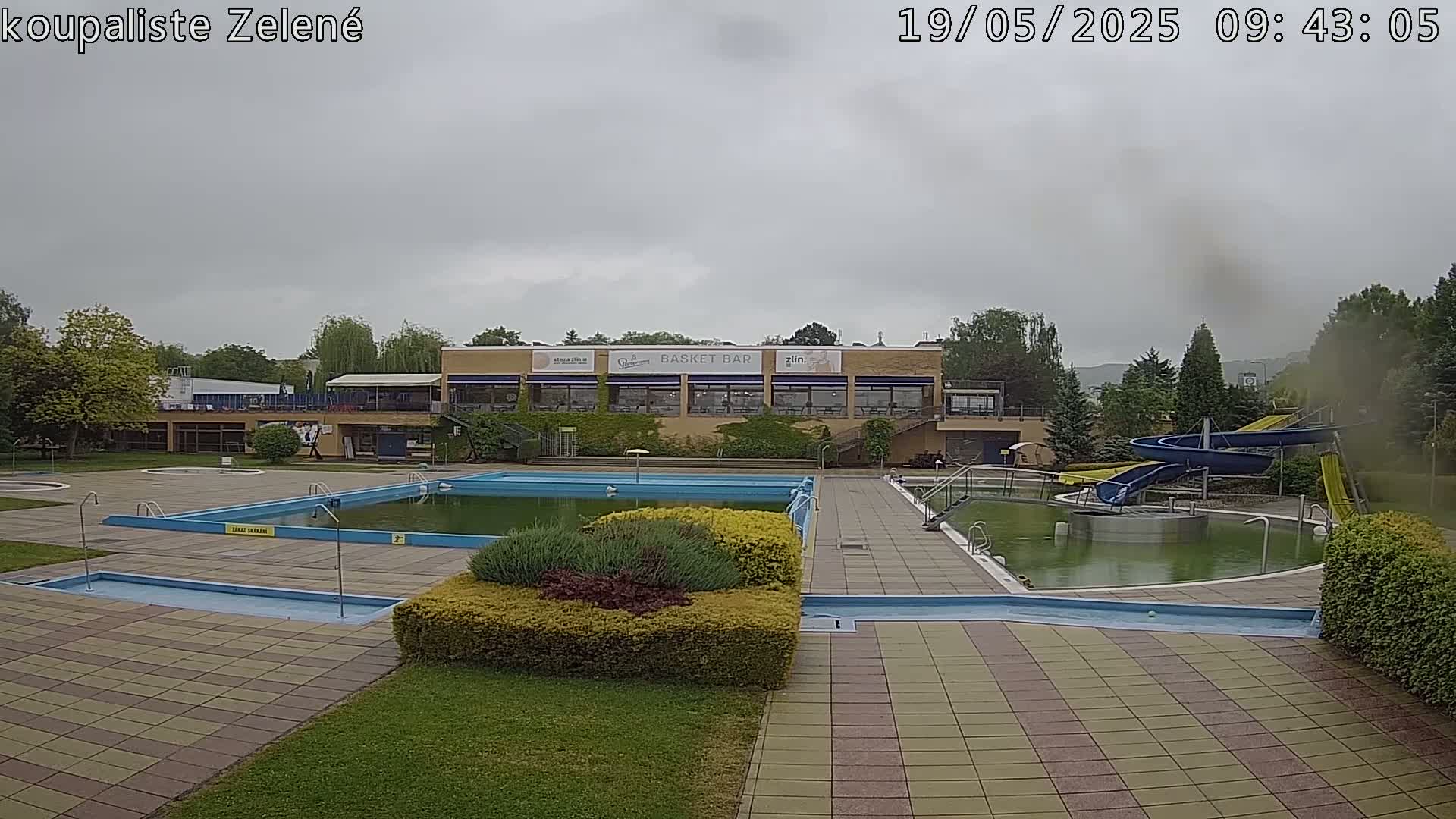 An outdoor swimming pool complex with multiple pools, water slides, and a building with a restaurant, under an overcast sky.
