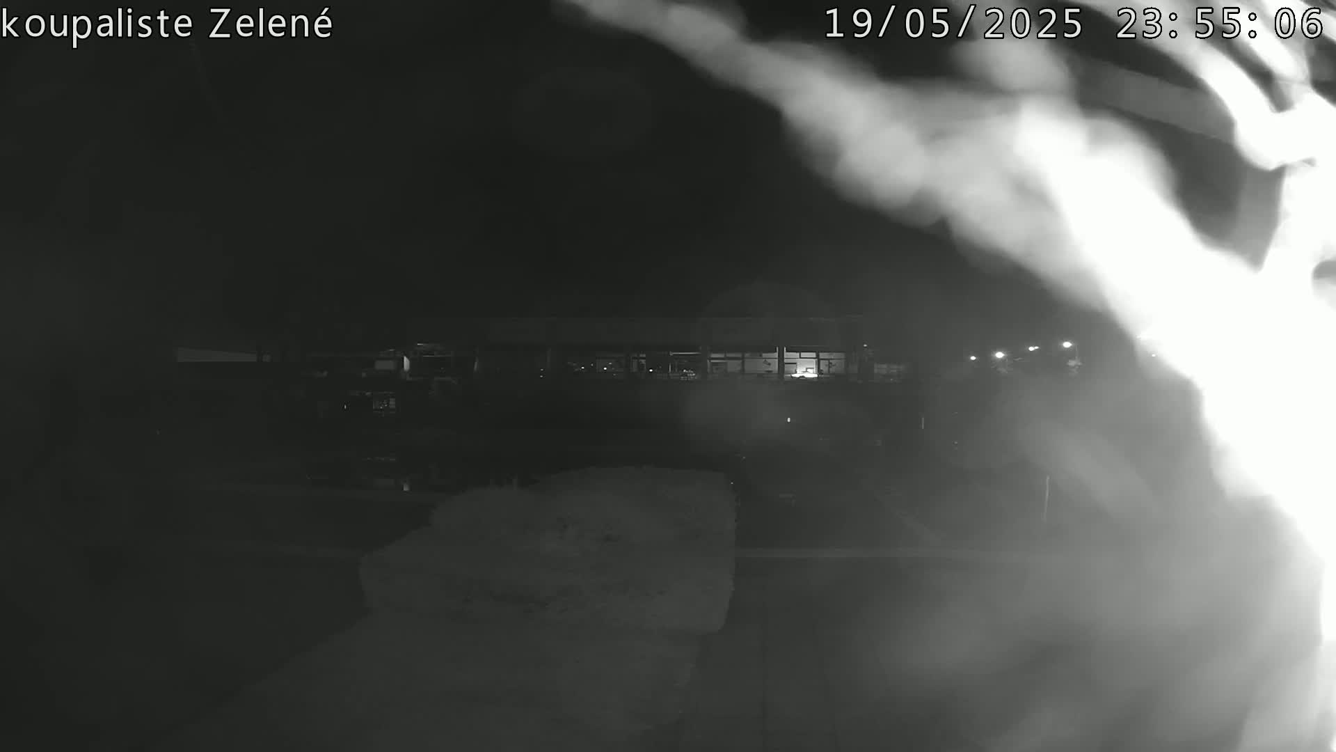 A nighttime, blurry, low-light security camera image shows a building with illuminated windows in the distance, partially obscured by fog or steam.