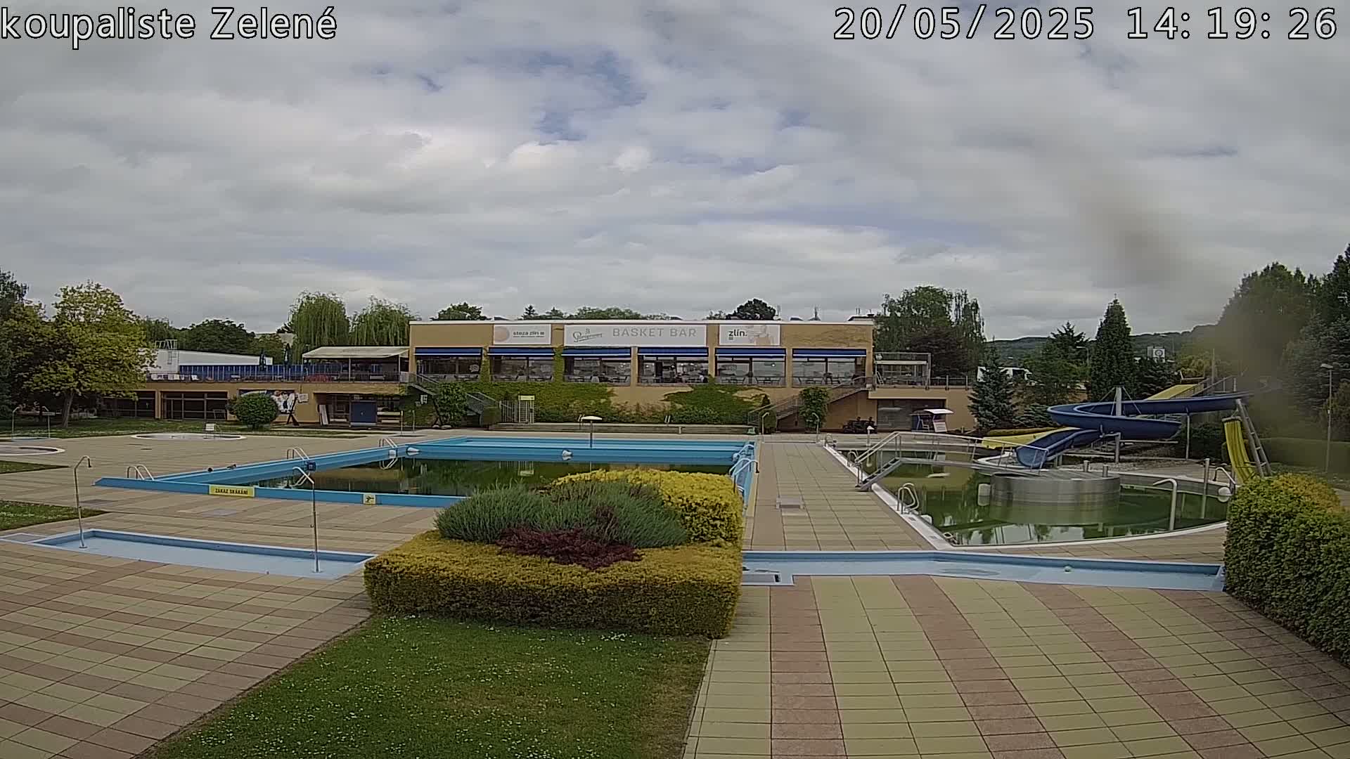 An outdoor swimming pool complex with a building, water slides, and cloudy skies.