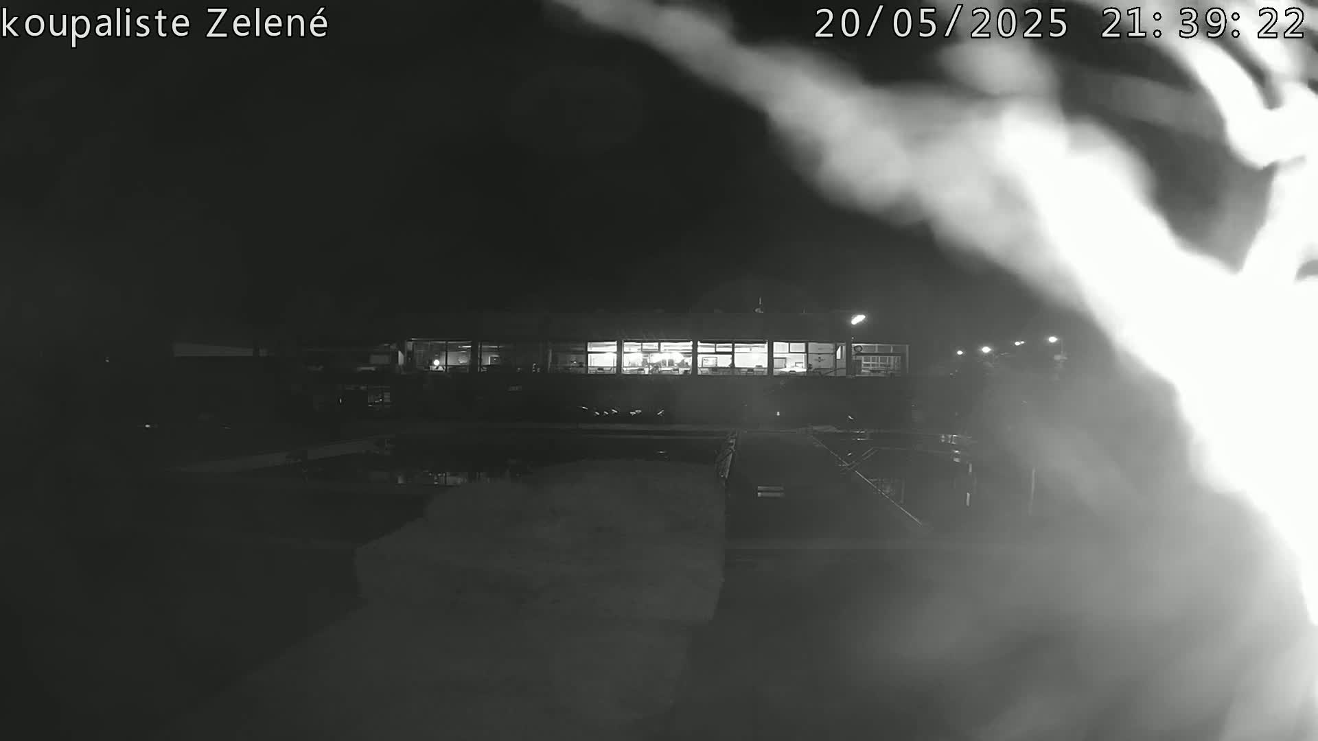 A nighttime, low-light view of a building with illuminated windows, partially obscured by fog or steam, near a body of water.