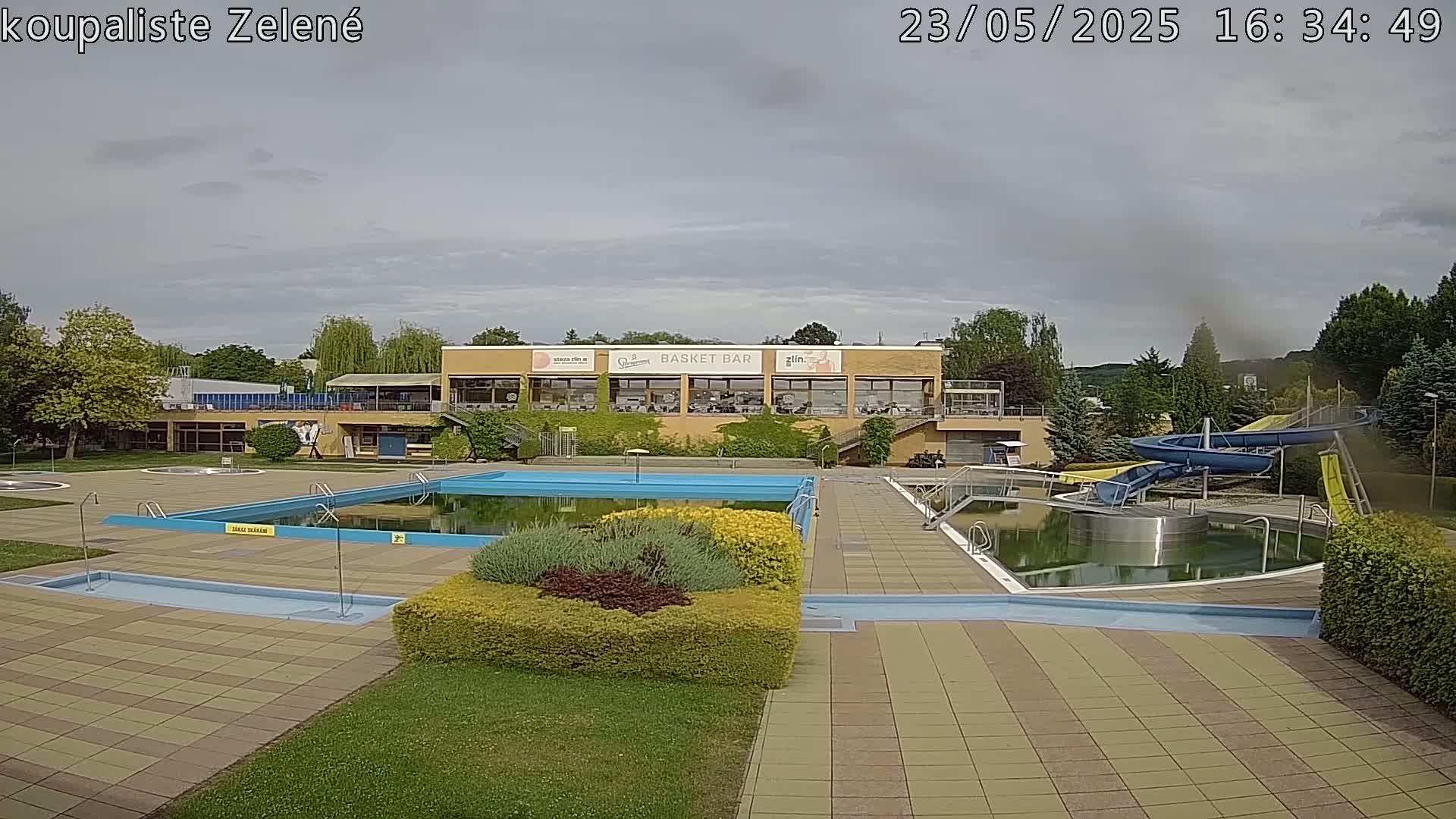 An outdoor pool complex with a water slide, under a mostly cloudy sky.