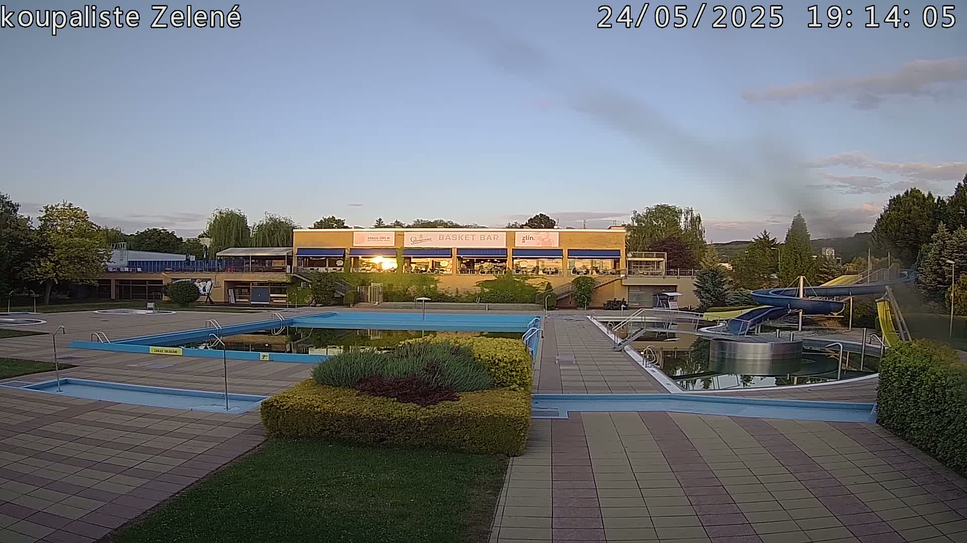 An outdoor pool complex with a building containing a restaurant, water slides, and a calm evening sky.