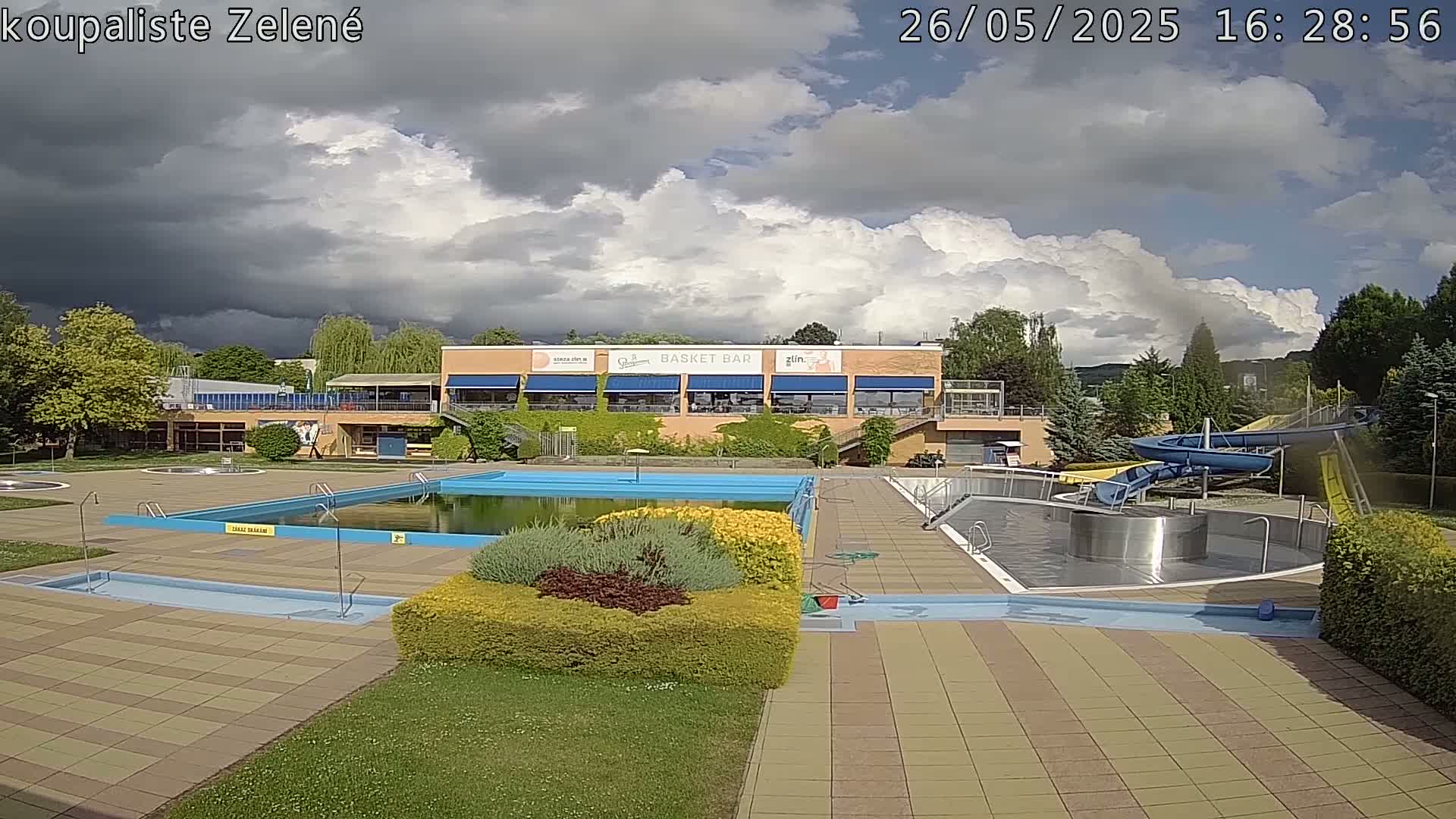 A swimming pool complex with a water slide is under a partly cloudy sky.