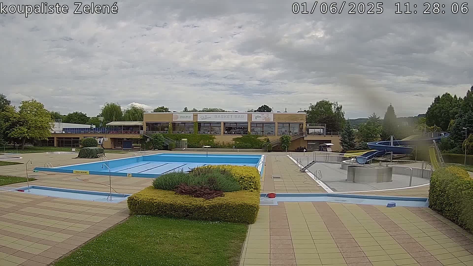 An outdoor swimming pool complex with a water slide and a building under a partly cloudy sky.