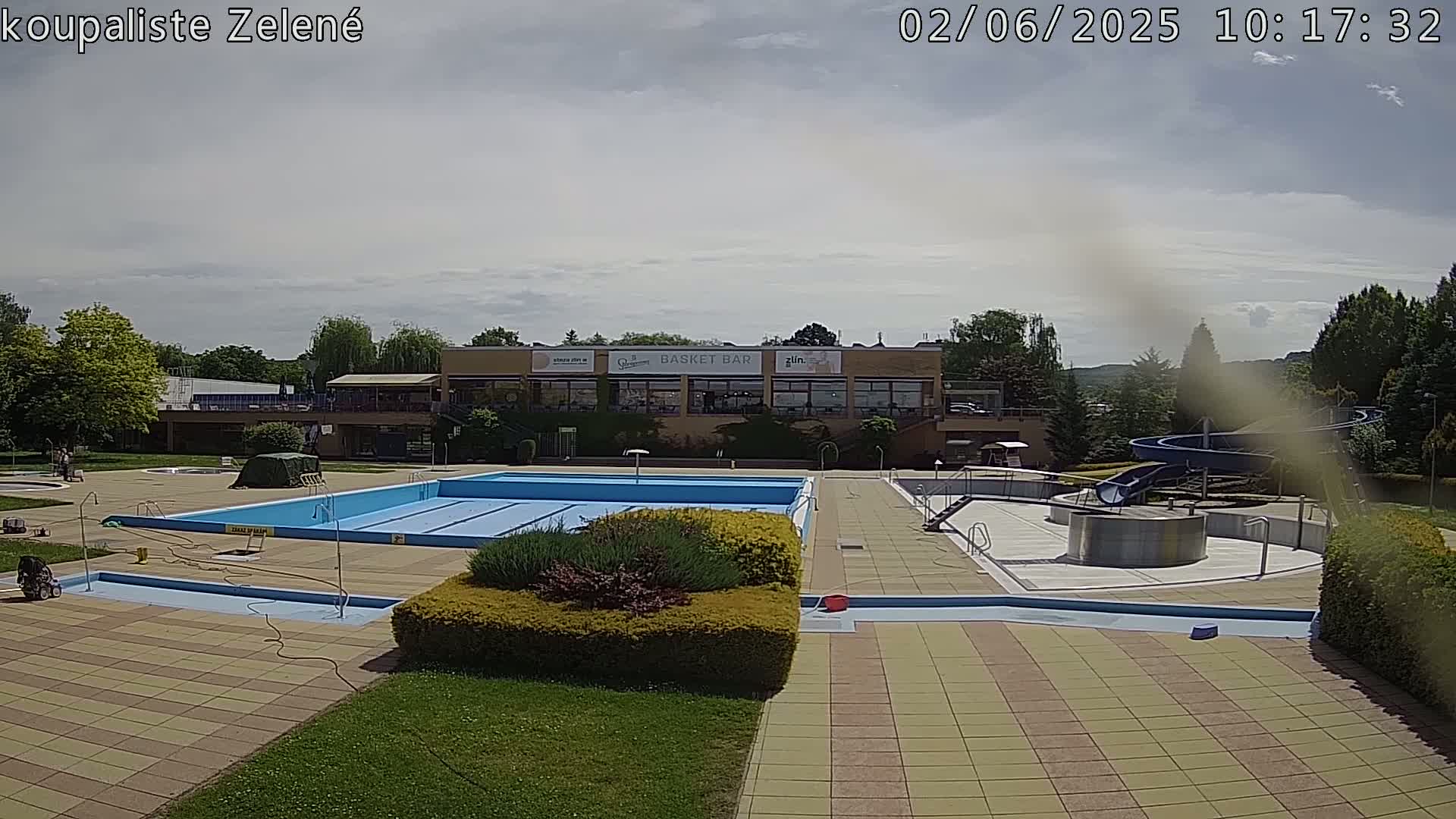 An outdoor swimming pool complex with a water slide, under a partly cloudy sky.