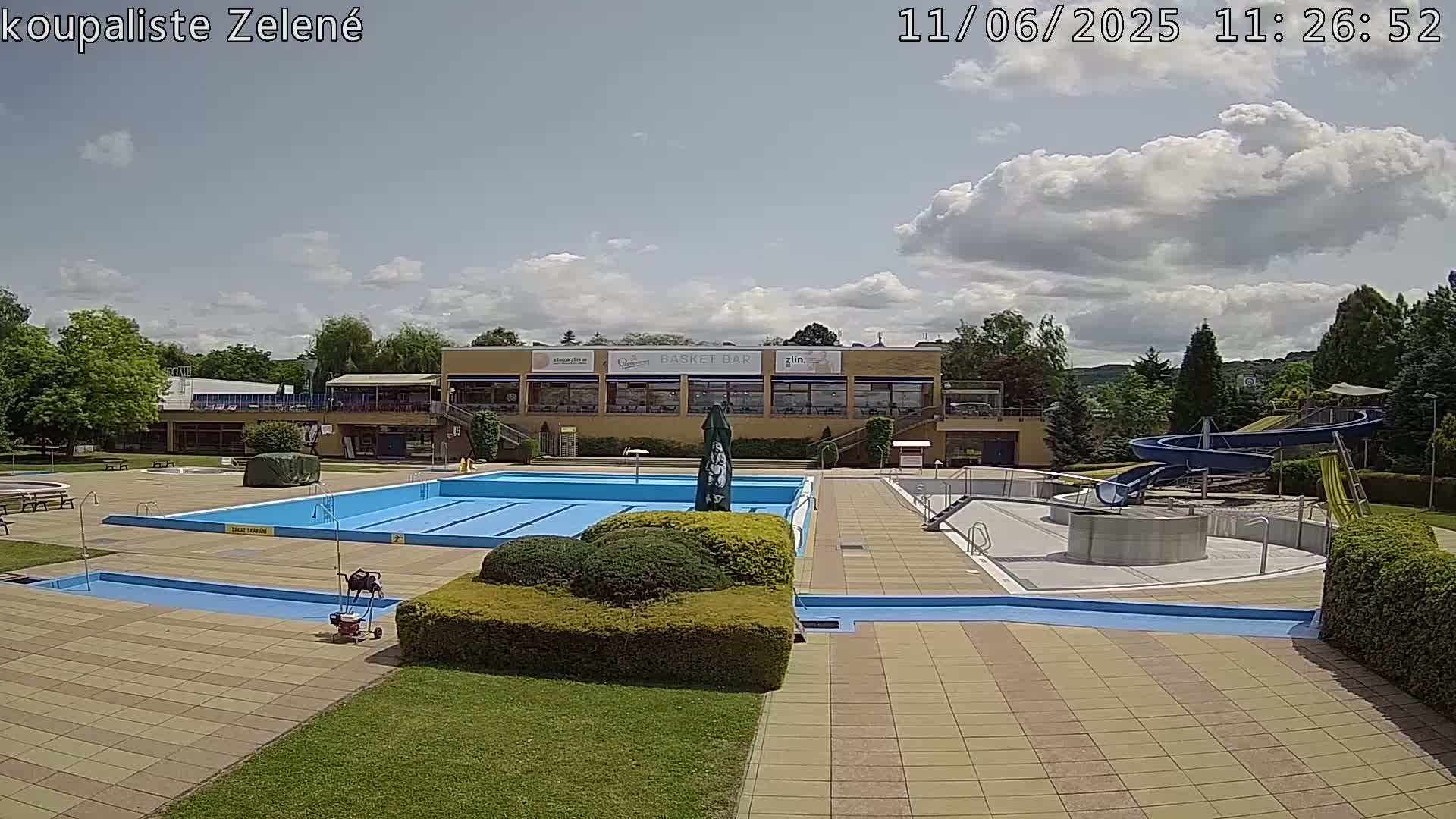 A swimming pool complex with a large pool, a smaller pool, and water slides, under a partly cloudy sky.