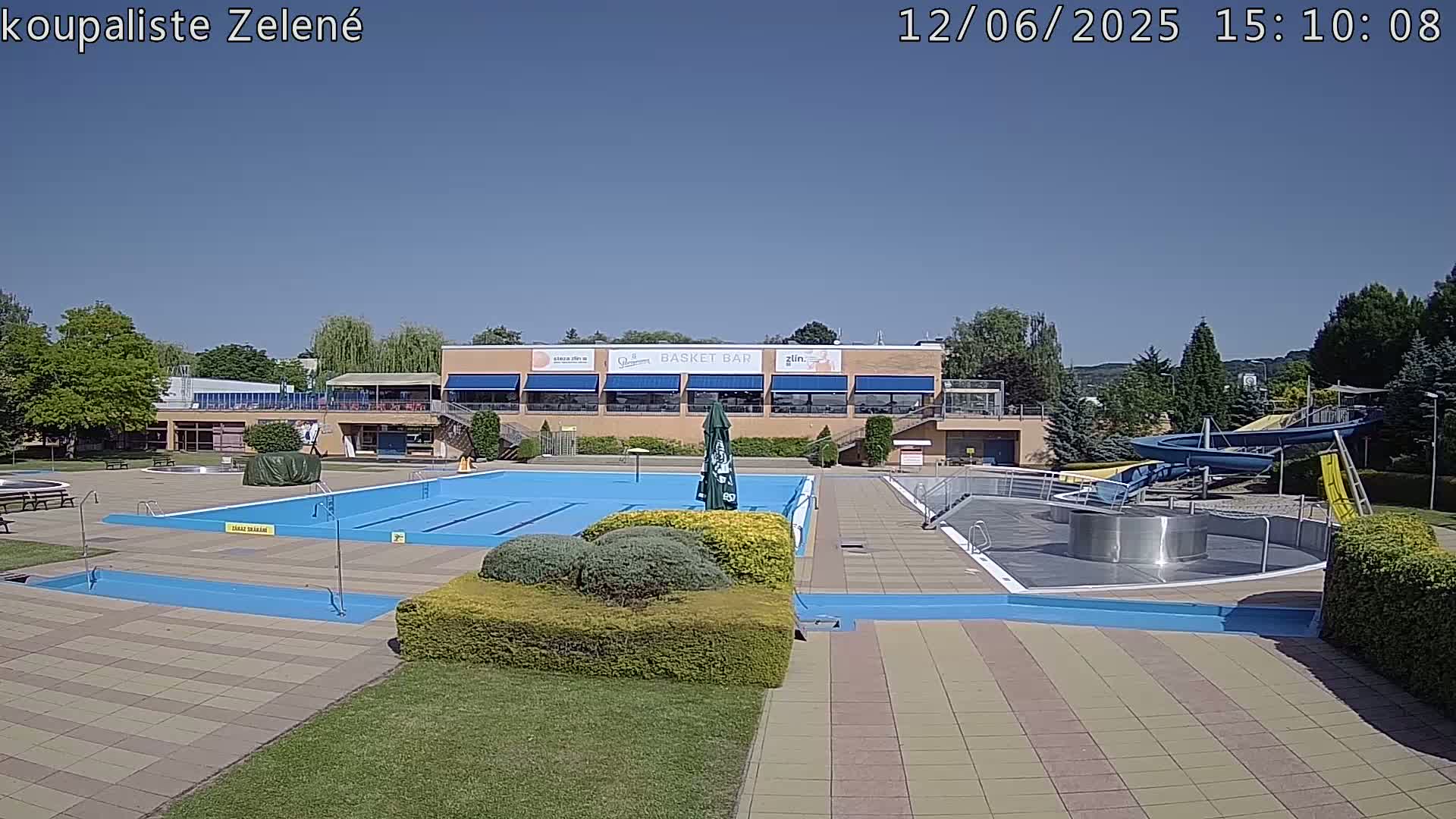 An outdoor swimming pool complex on a sunny day, featuring a large swimming pool, a smaller children's pool, and water slides.