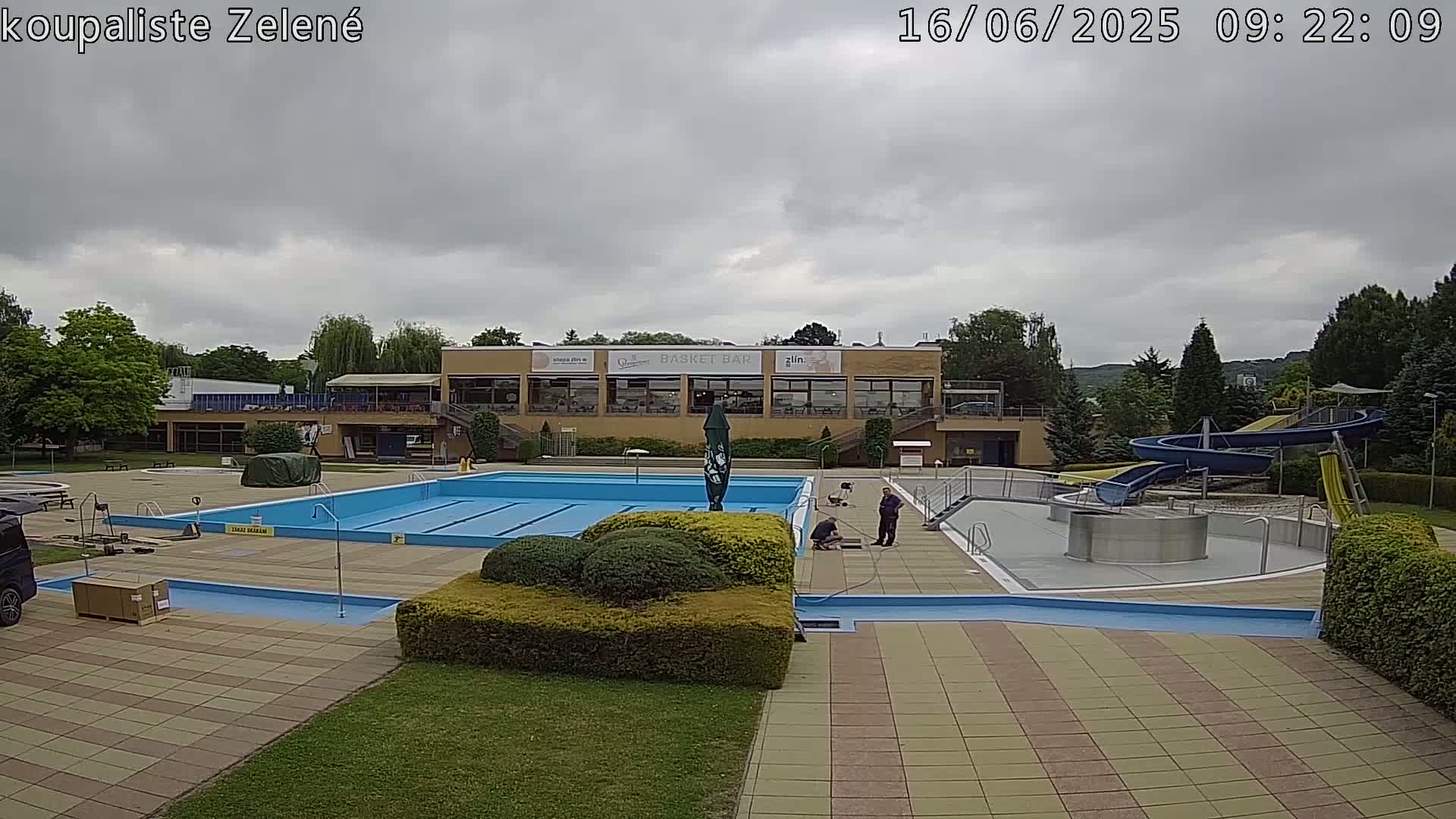 An outdoor swimming pool complex with a main pool, water slides, and a building under an overcast sky.