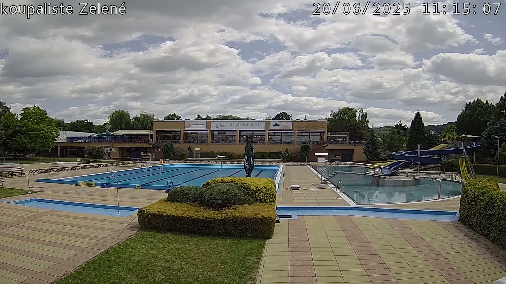 An outdoor swimming pool complex with a water slide, under a partly cloudy sky.