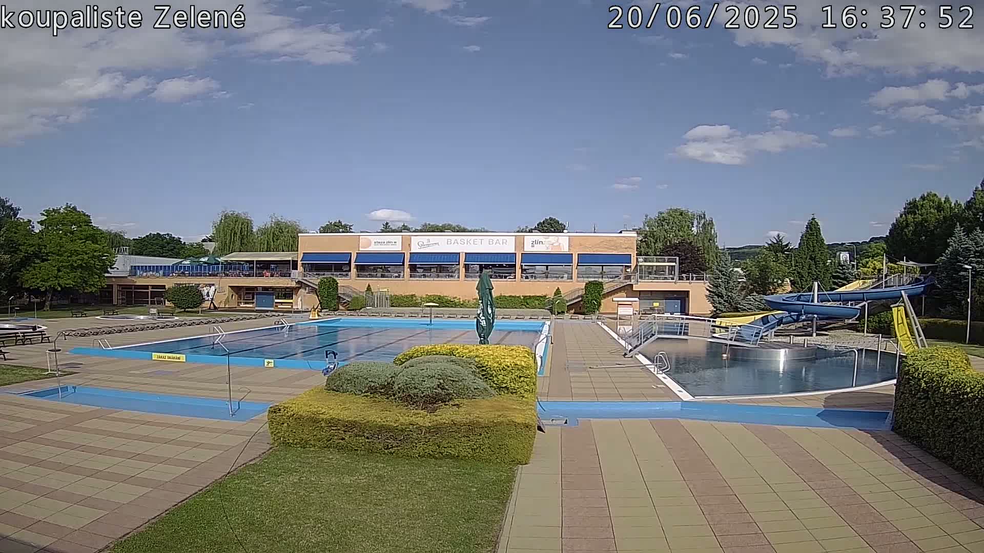An outdoor swimming pool complex with a water slide, under a partly cloudy sky.