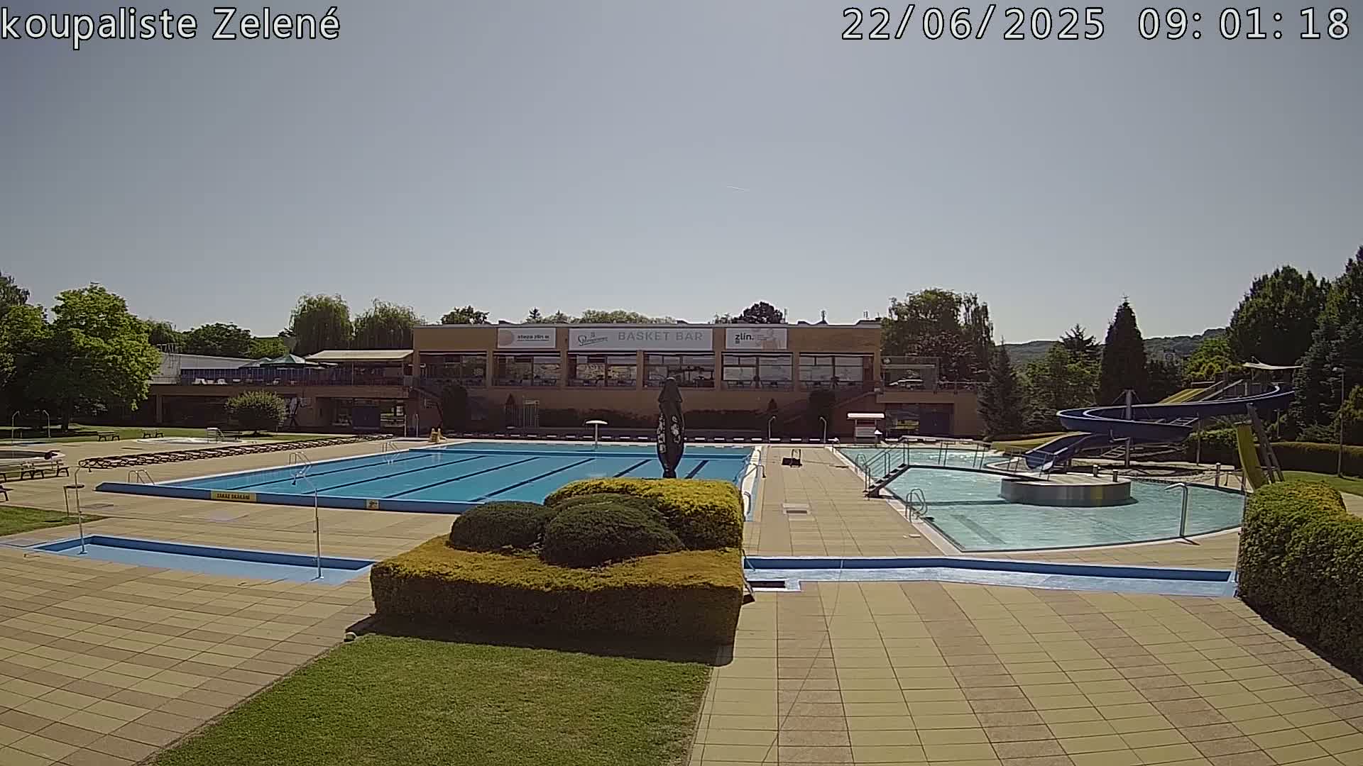 An outdoor swimming pool complex with a water slide is shown on a sunny day.