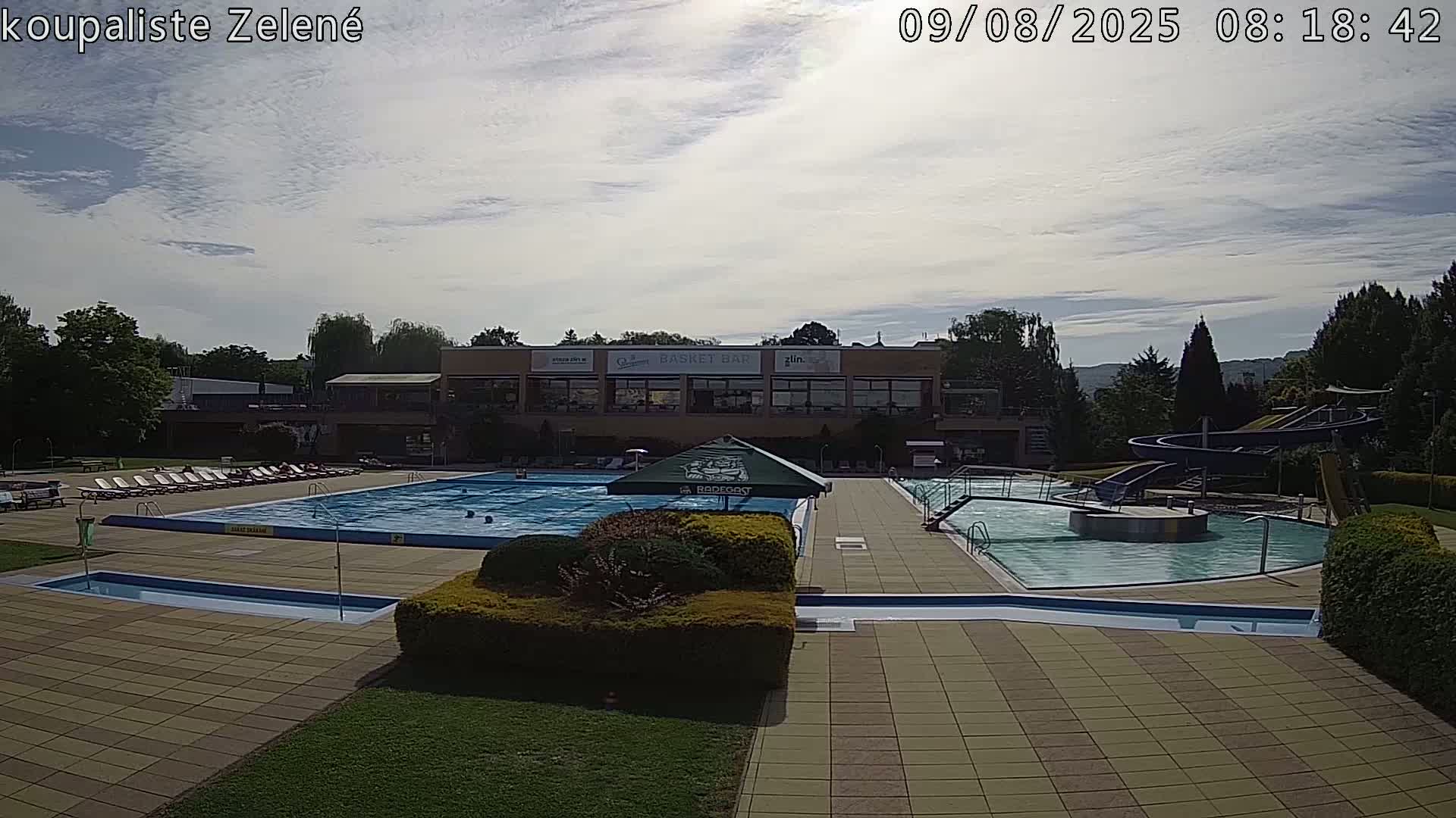 An outdoor swimming complex with multiple pools, water slides, and lounge chairs under a partly cloudy sky.