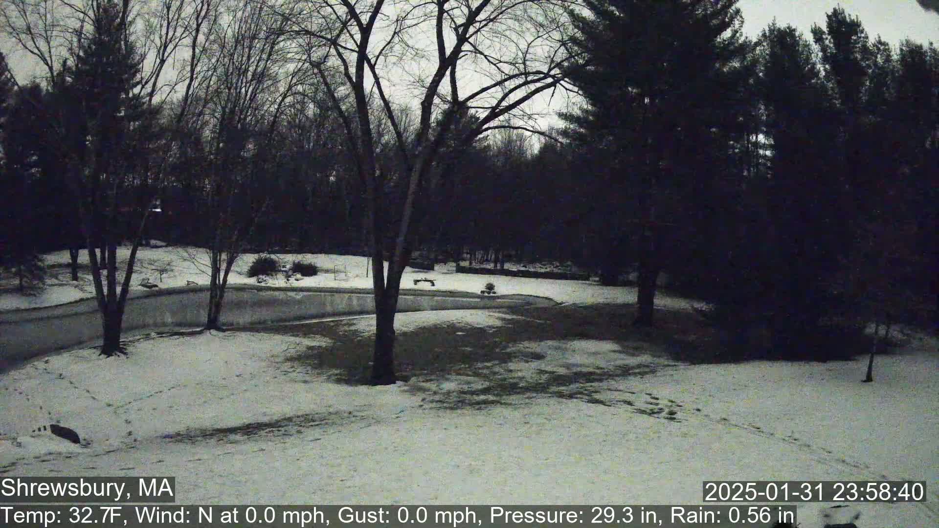 A snow-covered, dimly lit landscape with bare trees under a dark sky, showing light rain and a temperature of 32.7°F.