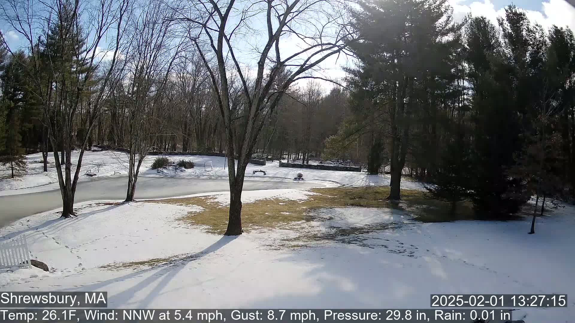 A snow-covered yard with bare trees and a partially frozen pond is visible under a partly sunny sky.