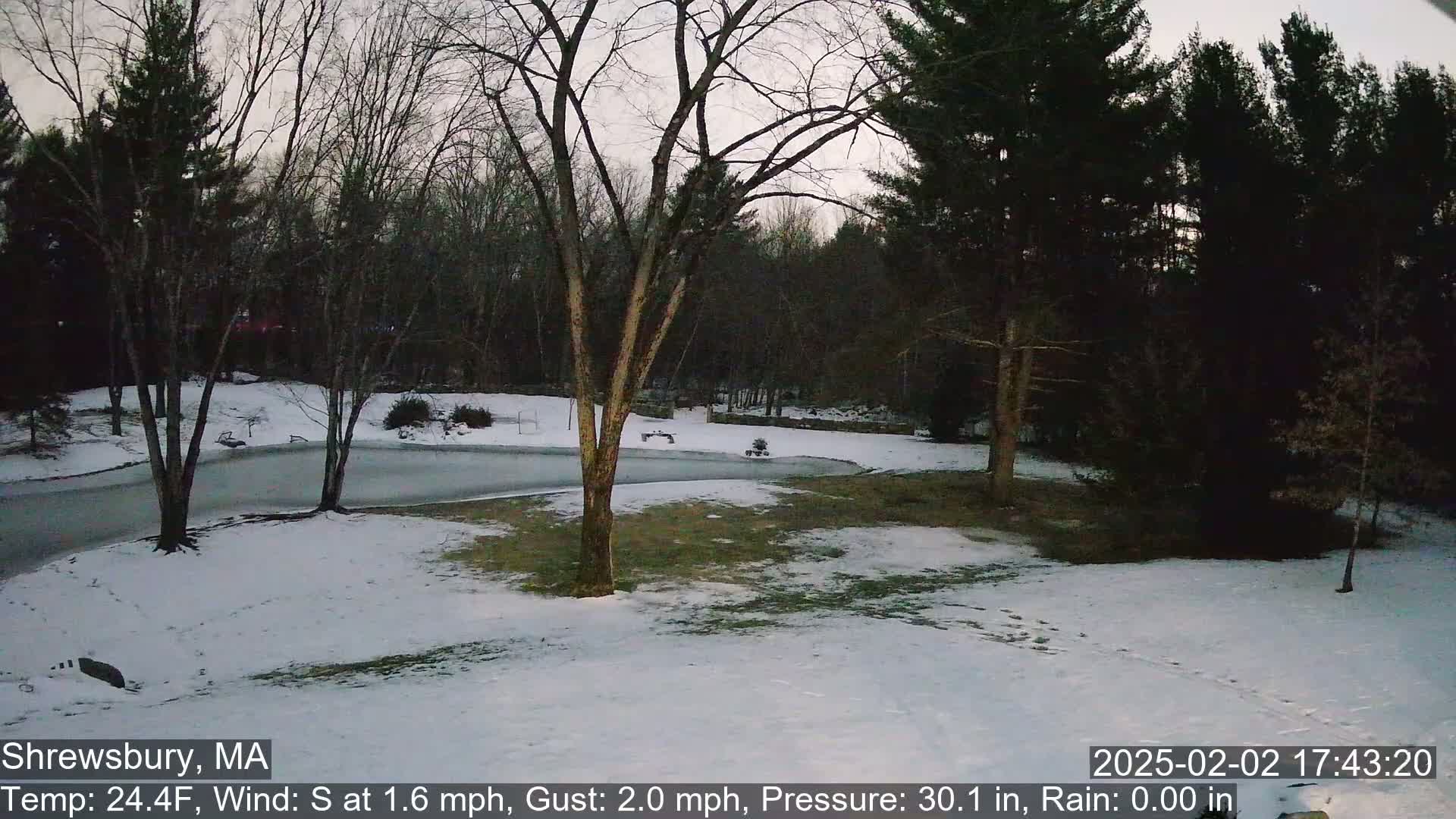 A snow-covered yard with bare trees and a paved driveway is visible under a twilight sky.