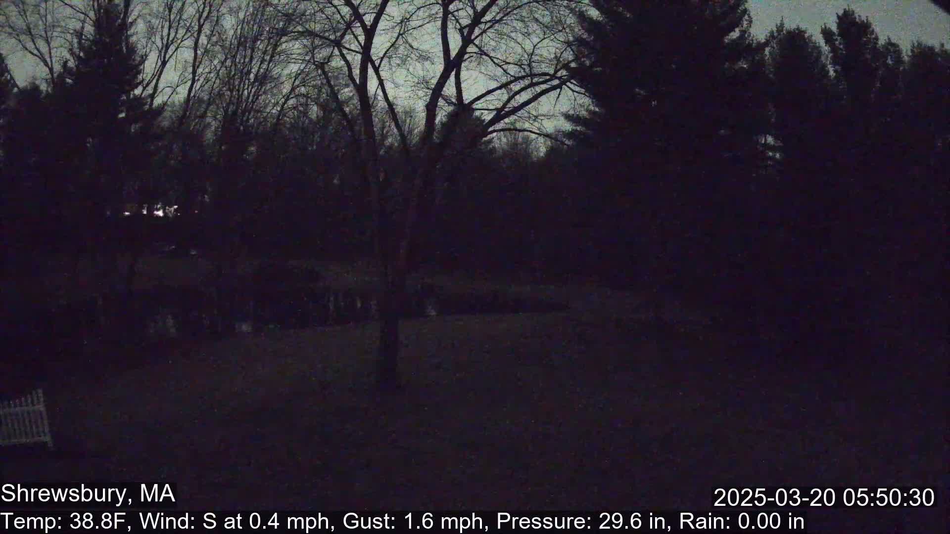 A dark nighttime scene shows a yard with bare trees and a white picket fence partially visible in the lower-left corner.