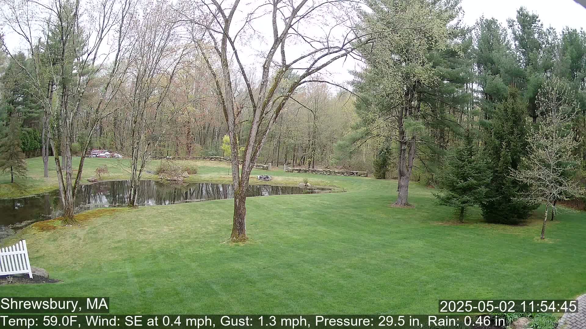 A grassy lawn with a pond, trees, and a stone wall is visible under an overcast sky.