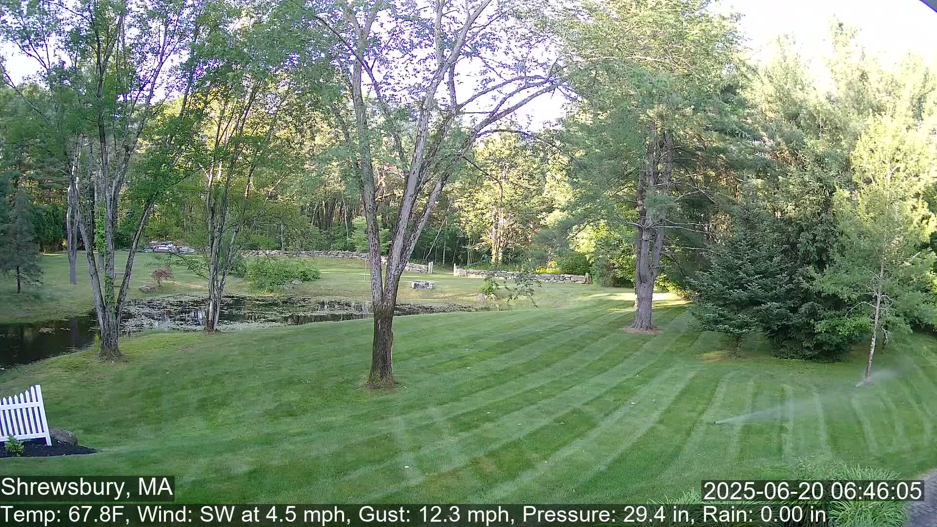 A neatly mown lawn stretches toward a pond and wooded area under a partly sunny sky.